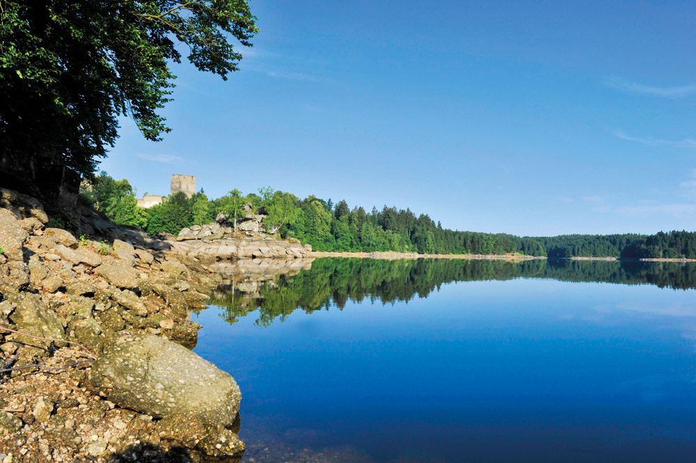 Kampsee Ottenstein mit ruhigem Wasser, bewaldeten Ufern und einer Burg im Hintergrund.