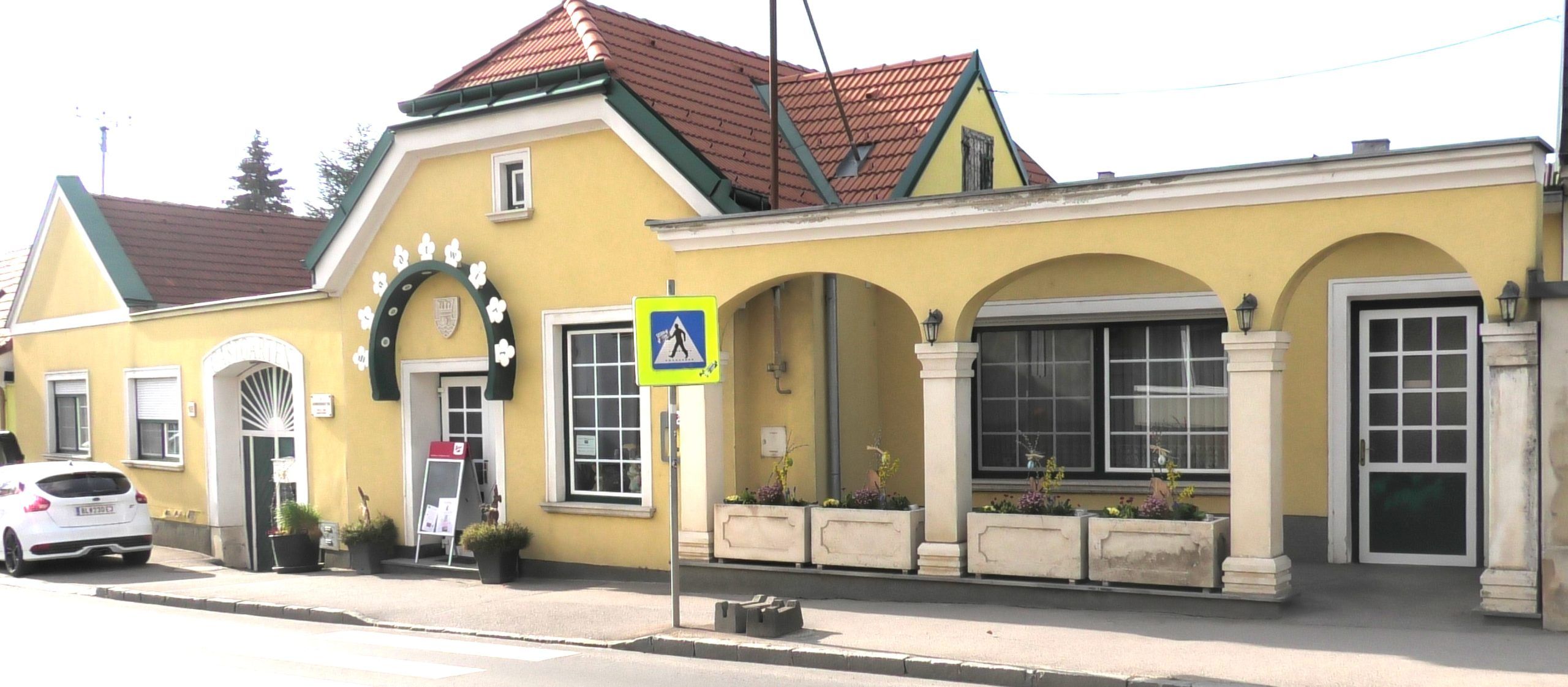 Außenansicht eines gelben Gebäudes mit Arkaden und rotem Dach.