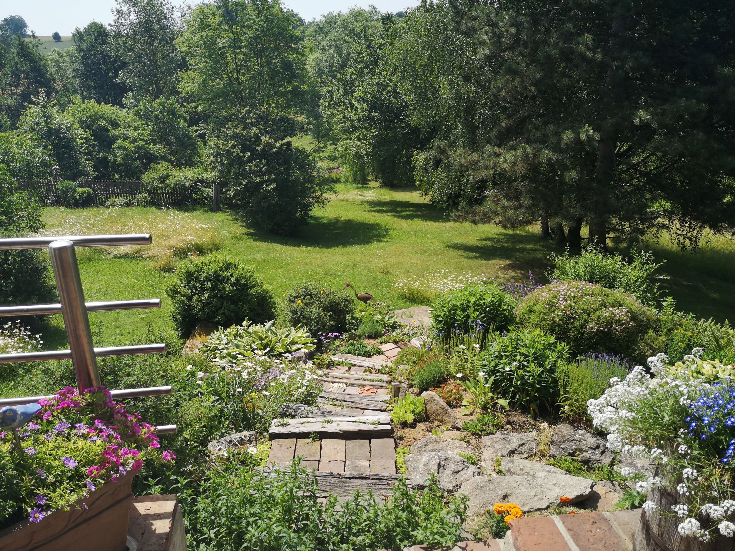 Ein gepflegter Garten mit Blumen, Büschen und einem Rasenbereich im Hintergrund.
