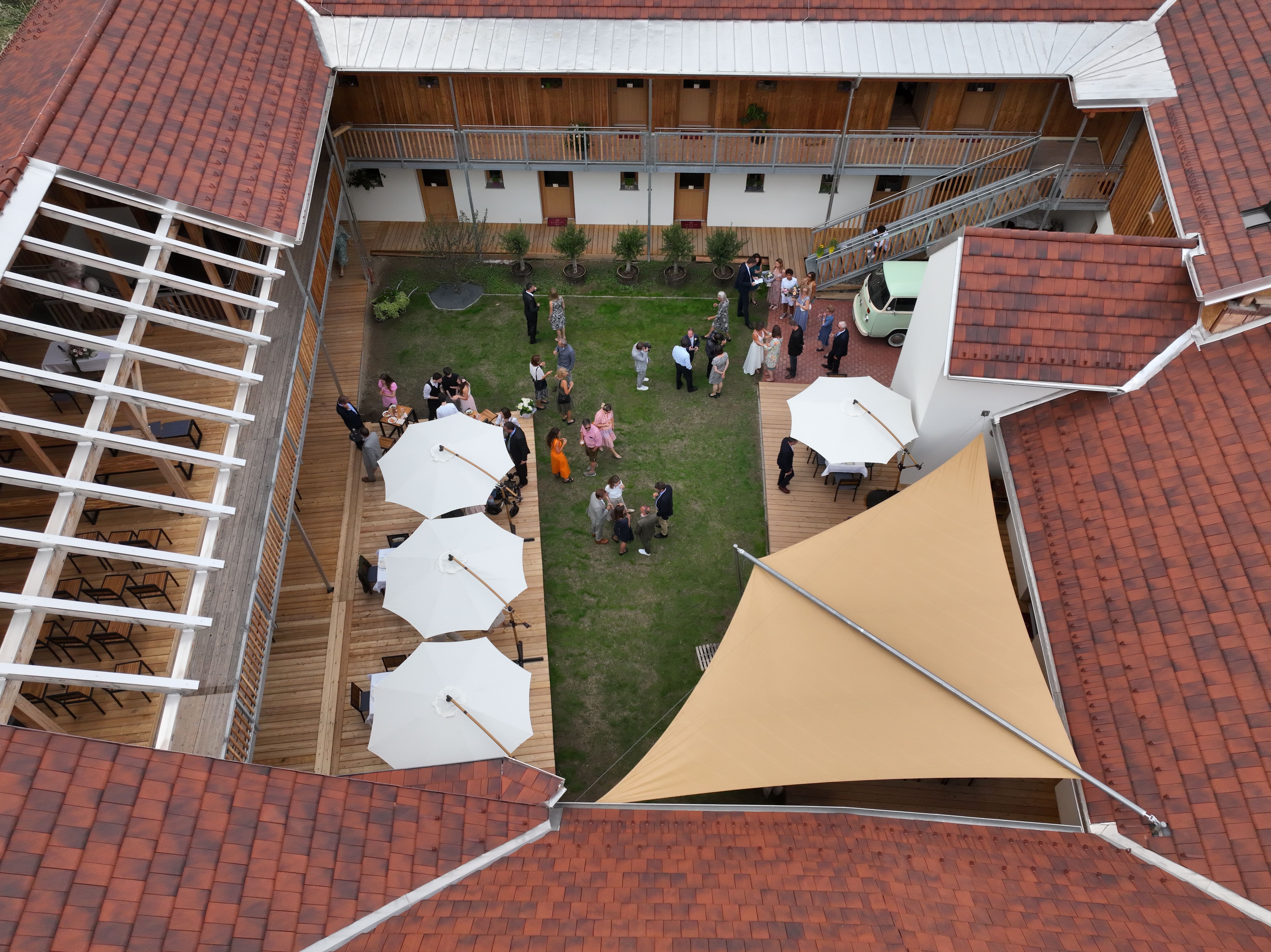 Blick aus der Vogelperspektive in den Innenhof mit grünem Rasen, weißen Sonnenschirmen und Gäste auf einem Empfang.