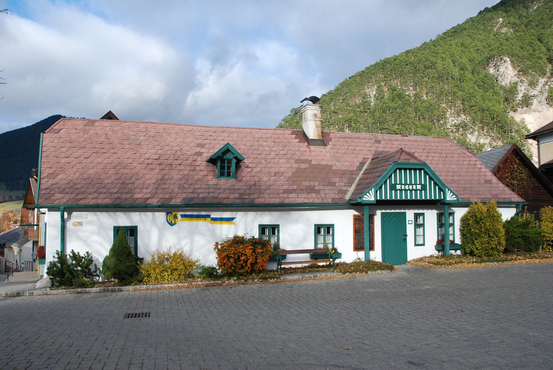 Schneebergmuseum Puchberg, ein traditionelles Gebäude mit grünem Dach und Schornstein, umgeben von Bergen und Bäumen.