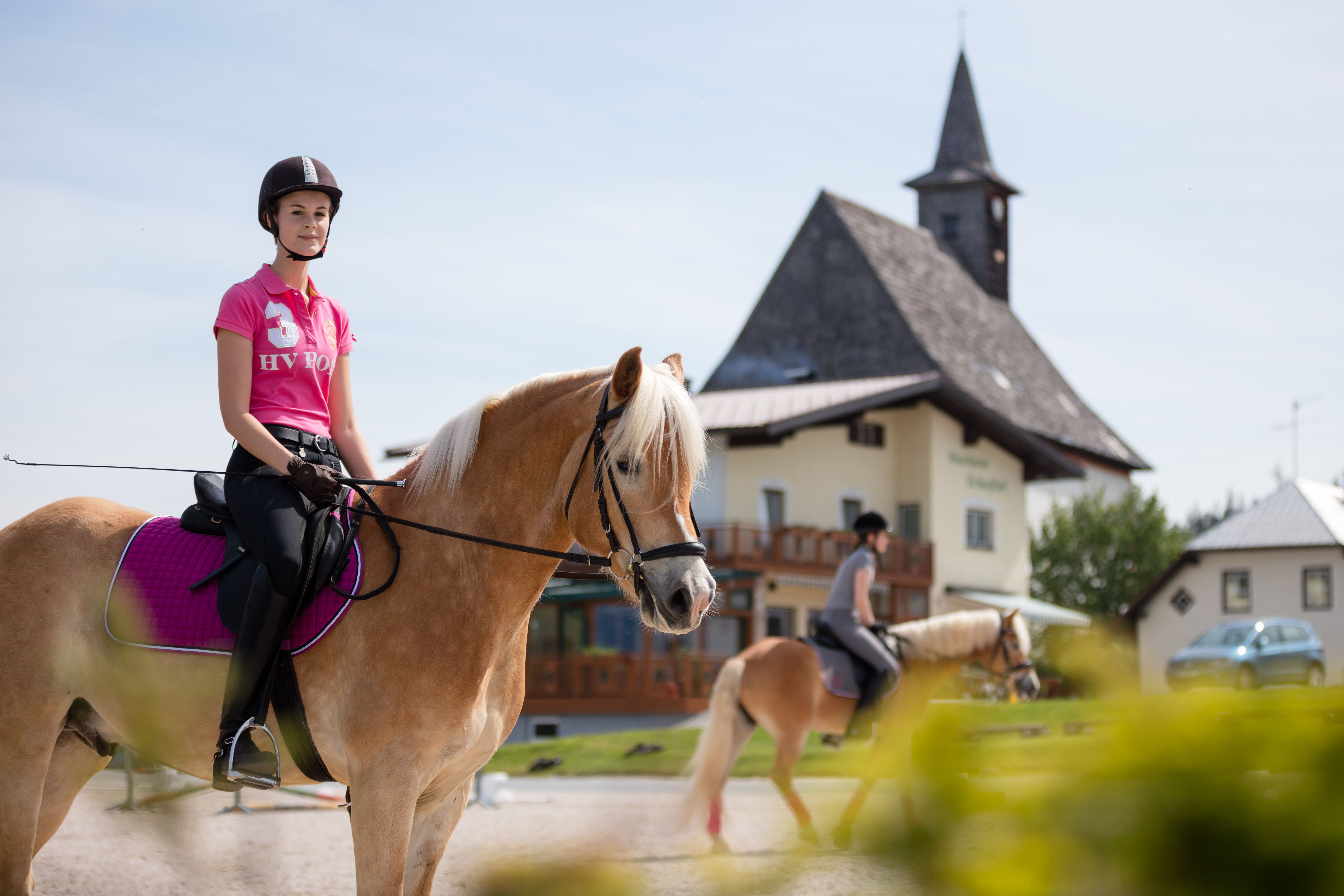 Zwei Reiterinnen auf Pferden vor einem Gebäude mit Turm.