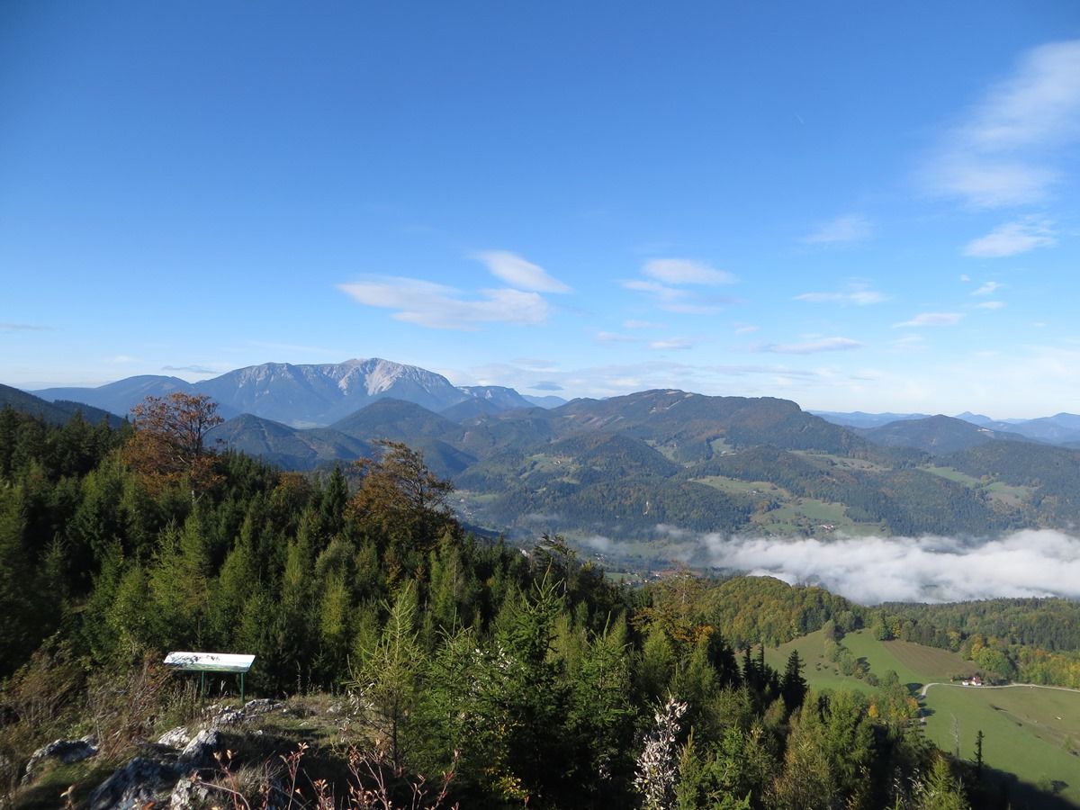 Panoramablick auf bewaldete Hügel und Berge unter blauem Himmel mit vereinzelten Wolken.