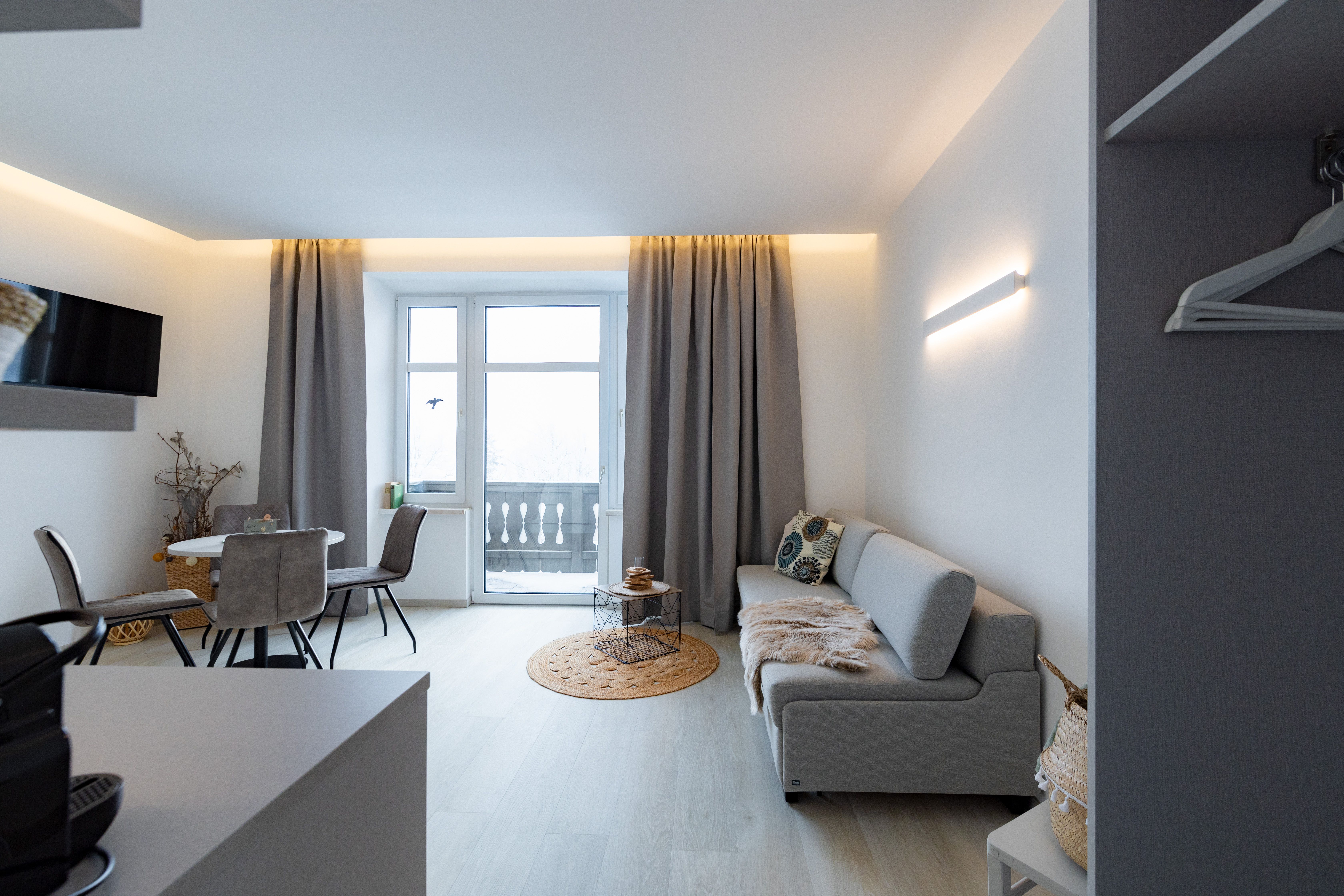 Modernes Wohnzimmer mit grauem Sofa, Esstisch und Balkon.