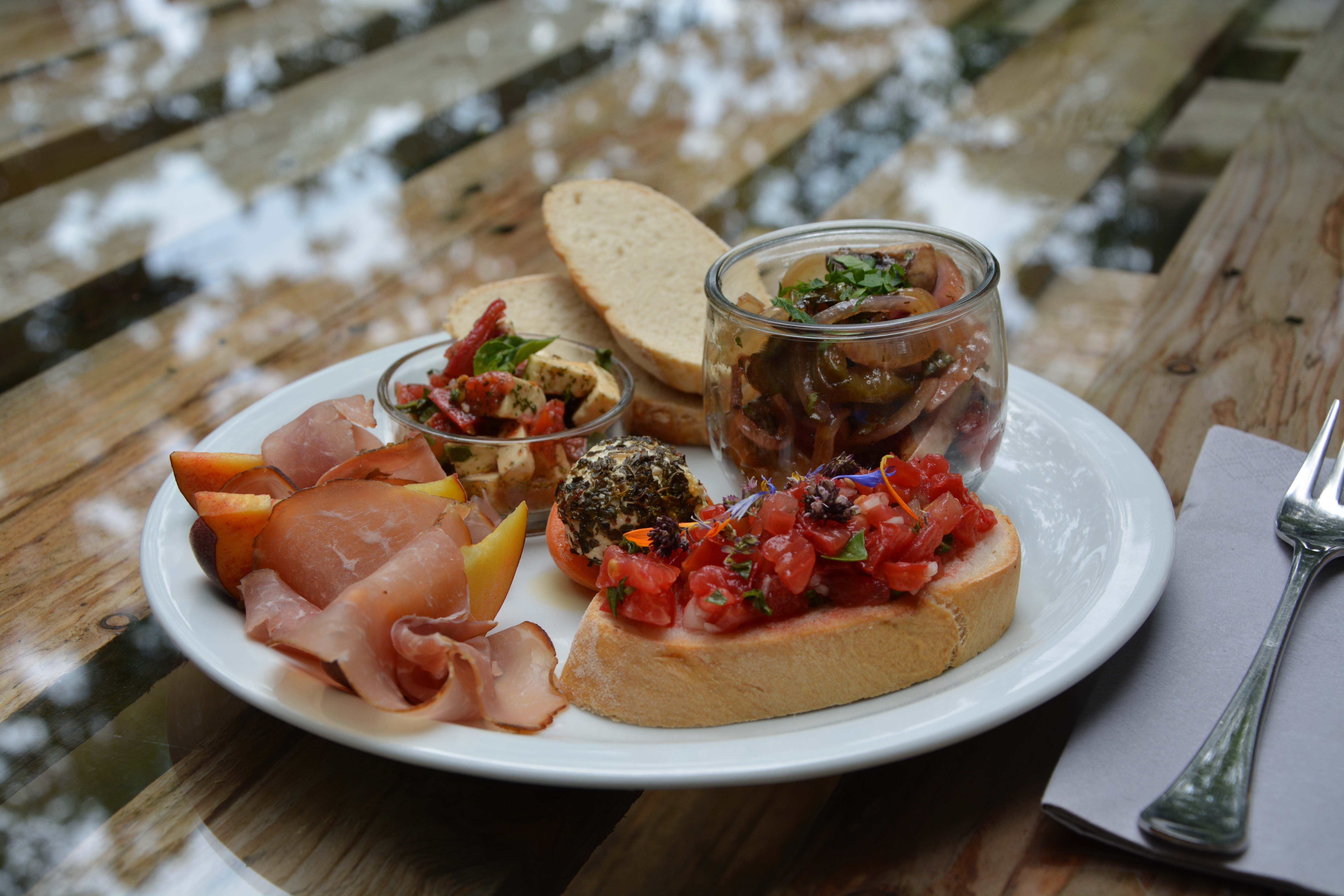 Ein Teller mit Brot, Schinken, Antipasti, Bruschetta und Obst auf einem Holztisch.