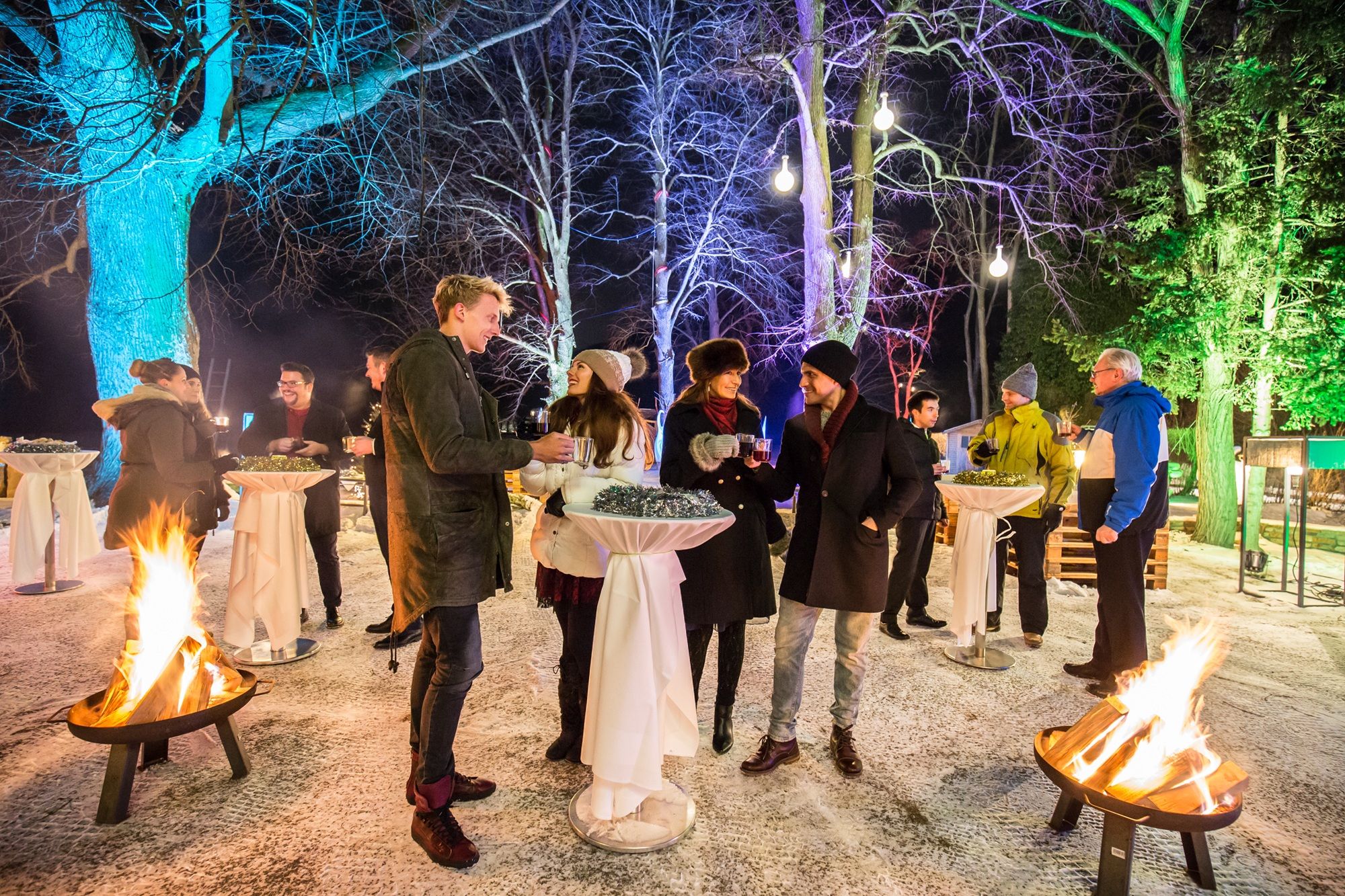 Menschen bei einer Weihnachtsfeier im winterlichen Wienerwald mit Punsch und Feuerkörben