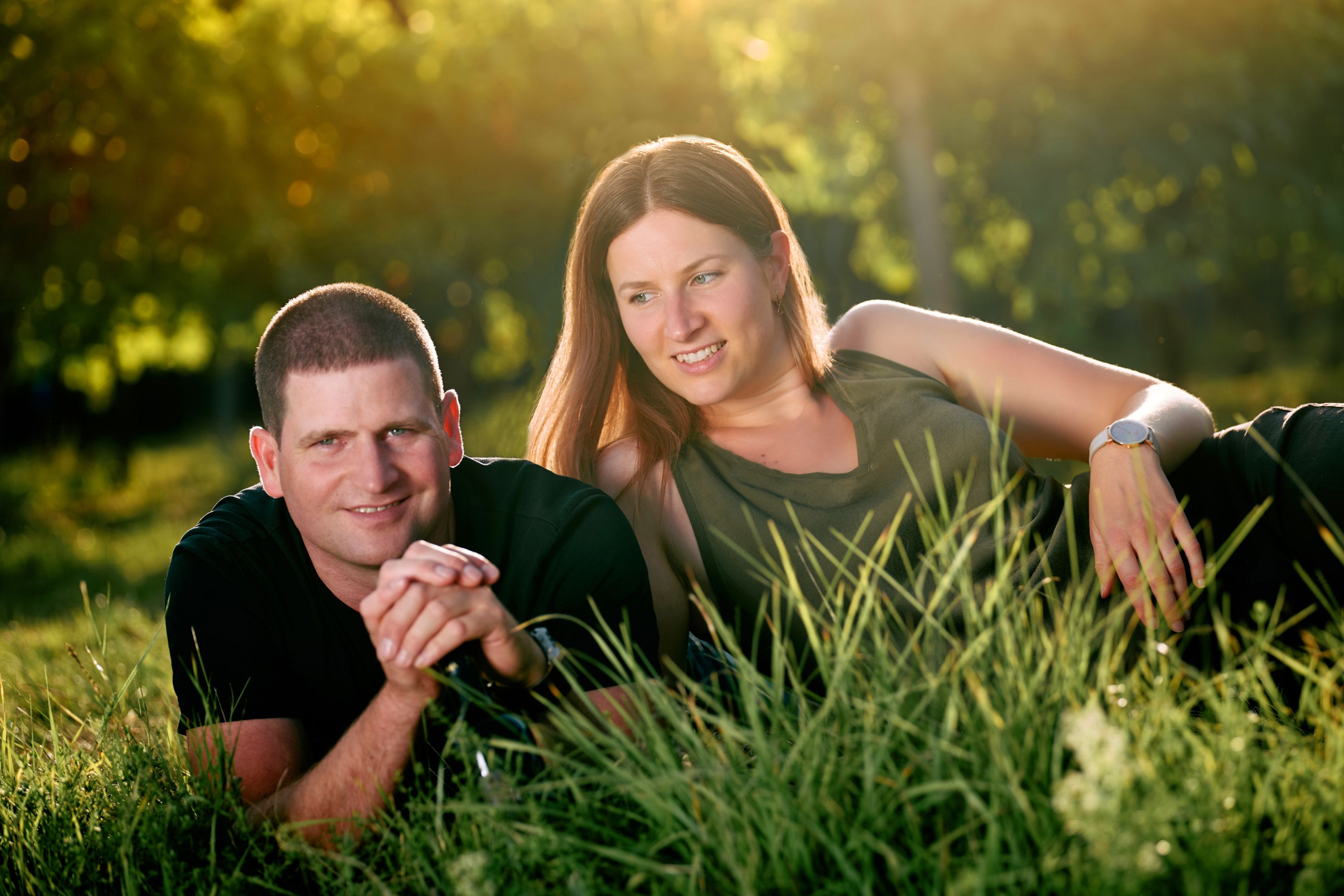 Ein Mann und eine Frau liegen entspannt im Gras, umgeben von grüner Natur und Sonnenlicht.