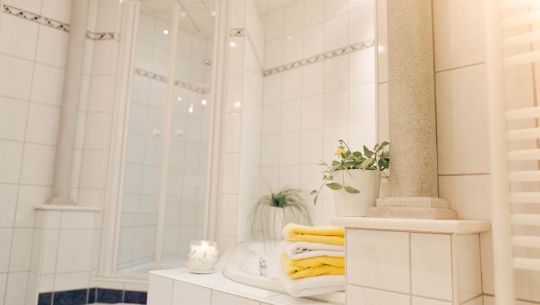 Modernes Badezimmer mit weißen Fliesen, gelben Handtüchern und Pflanzen.