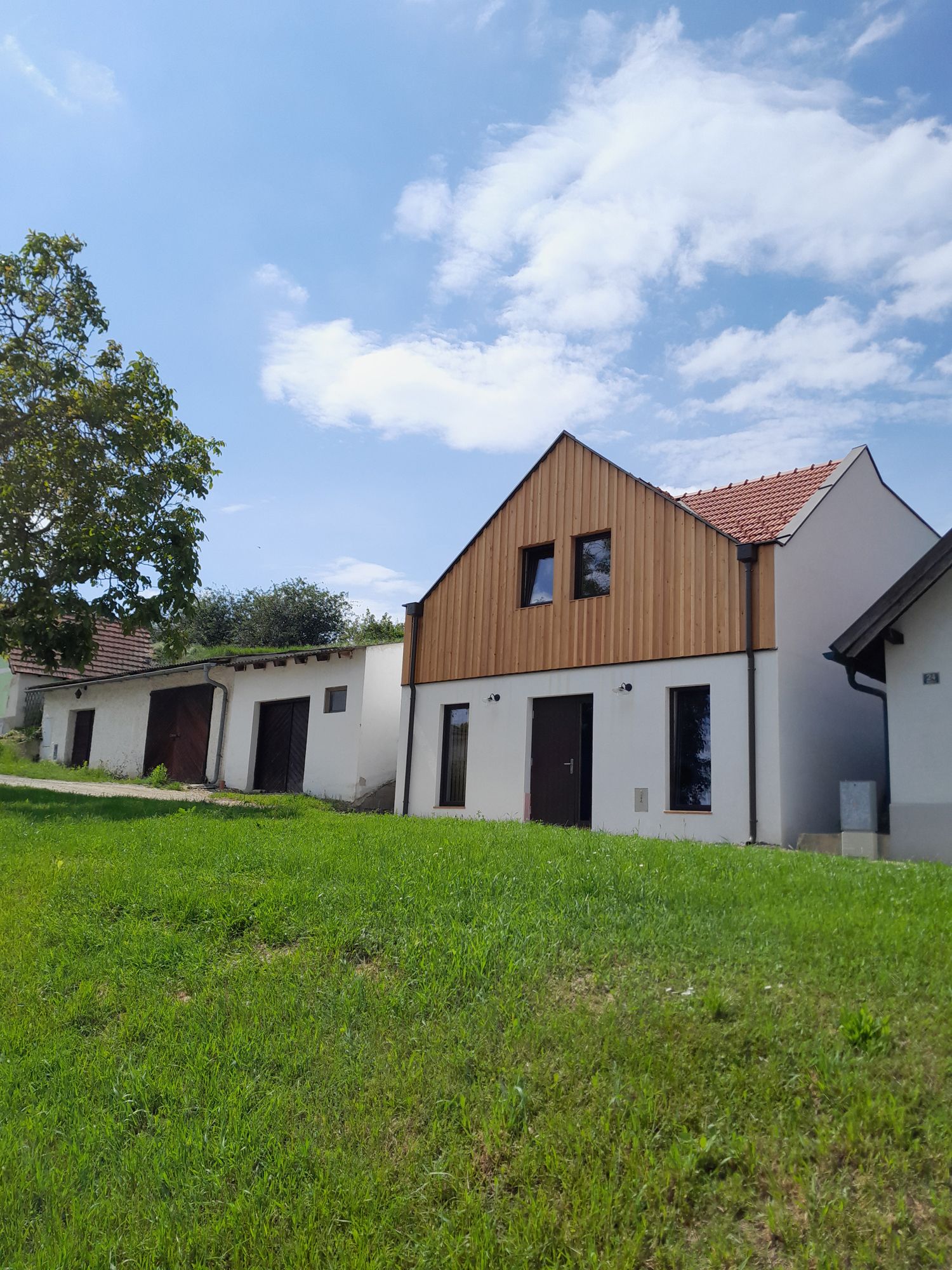 Ein modernes Gebäude mit Holzfassade und roten Dachziegeln steht auf einem grünen Hügel unter blauem Himmel.