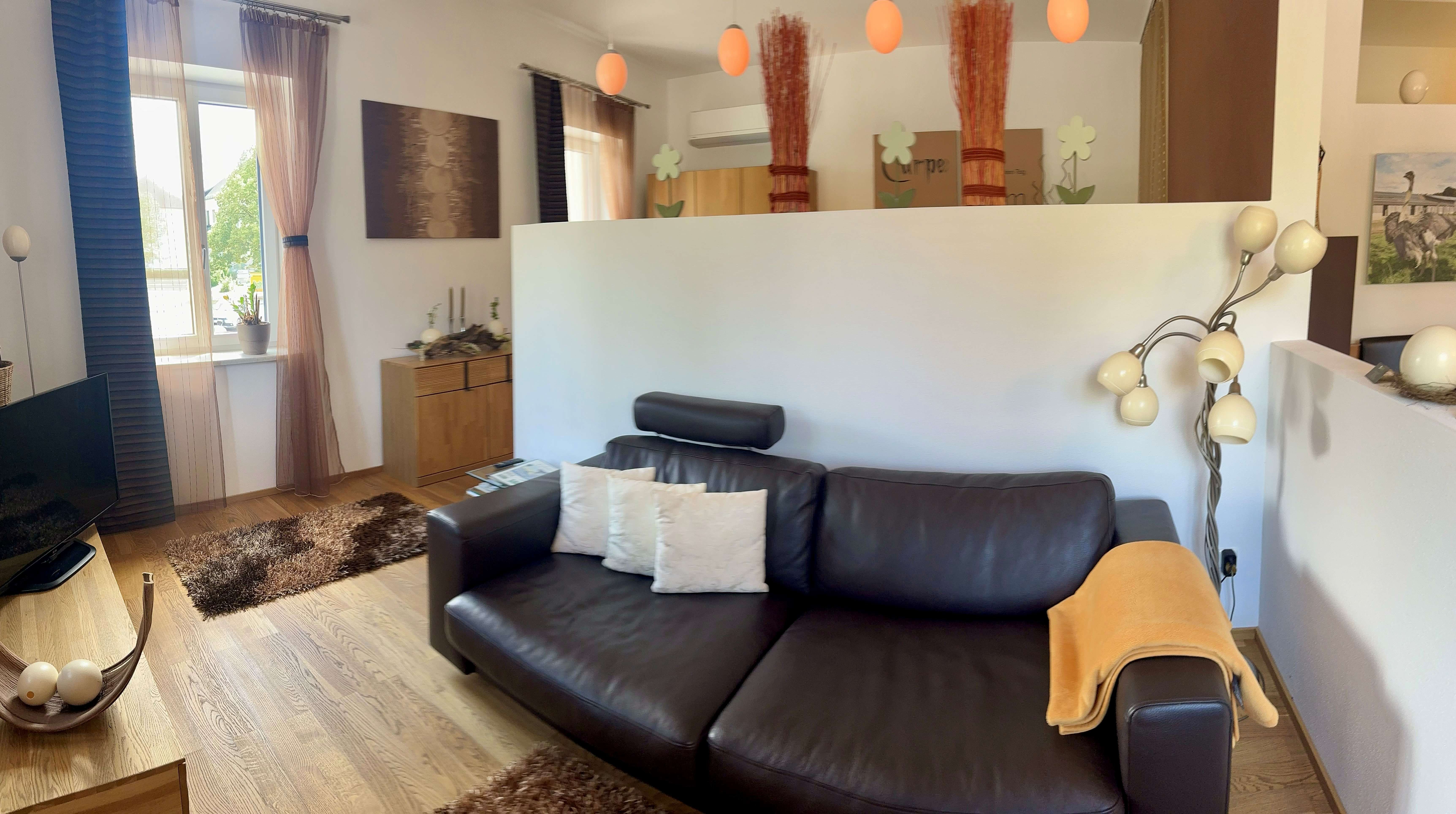 Modern eingerichtetes Wohnzimmer mit Ledersofa, Stehlampe und dekorativen Elementen.