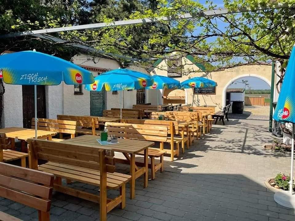 Ein sonniger Gastgarten mit Holzbänken und blauen Sonnenschirmen.