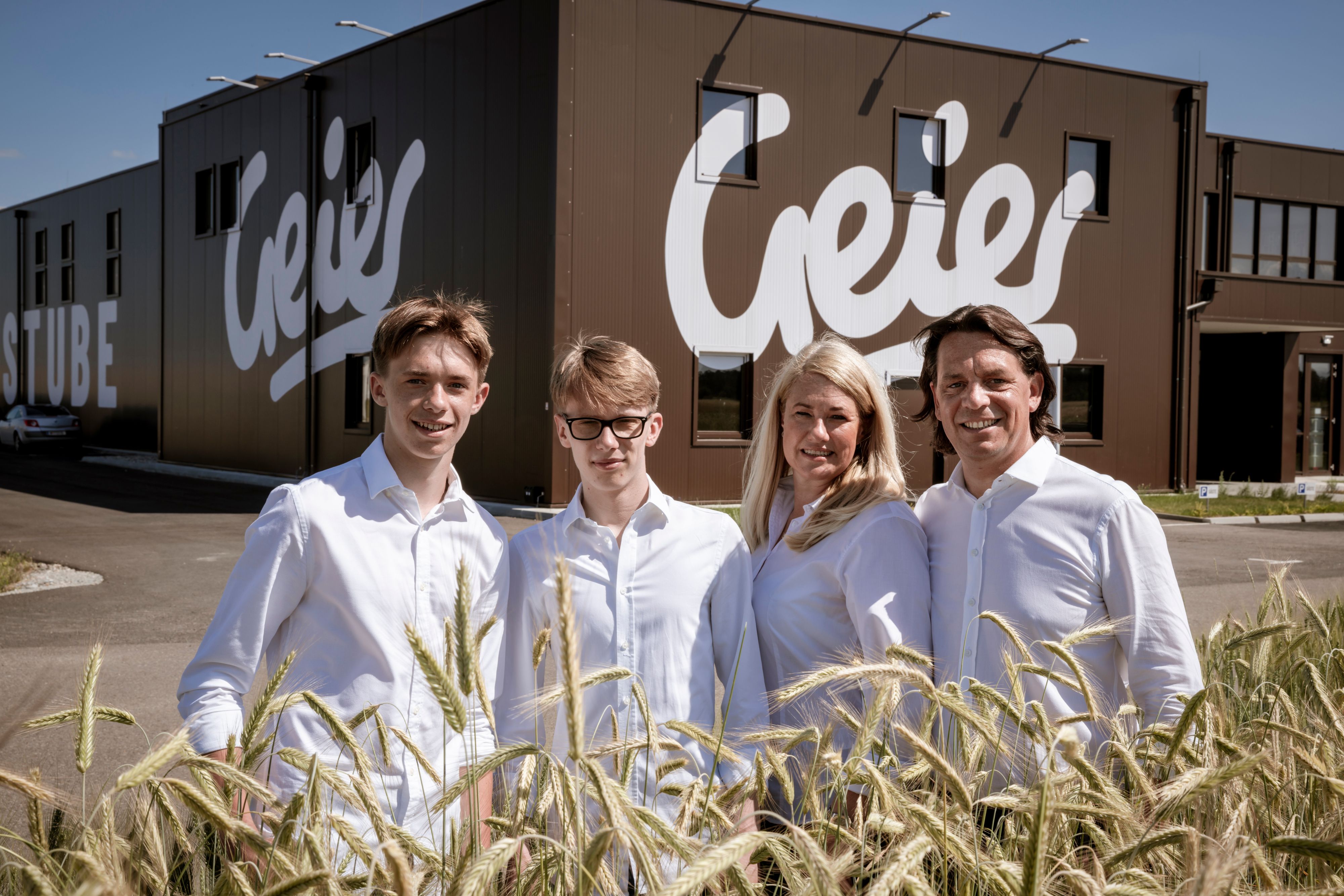 Vier Personen in weißer Kleidung stehen vor einem Gebäude mit der Aufschrift 'Geier'.