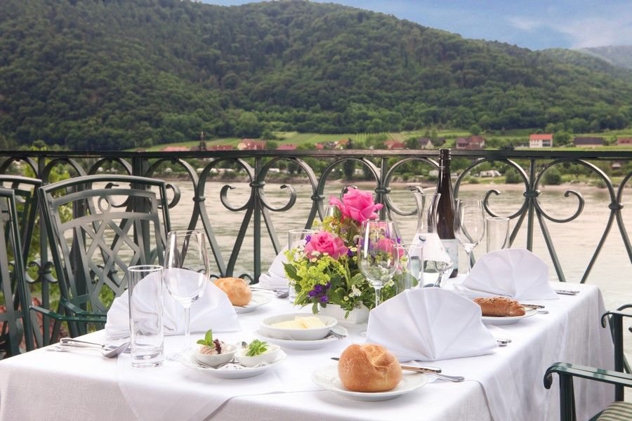 Gedeckter Tisch auf einer Terrasse mit Blick auf die Donau und bewaldete Hügel im Hintergrund.