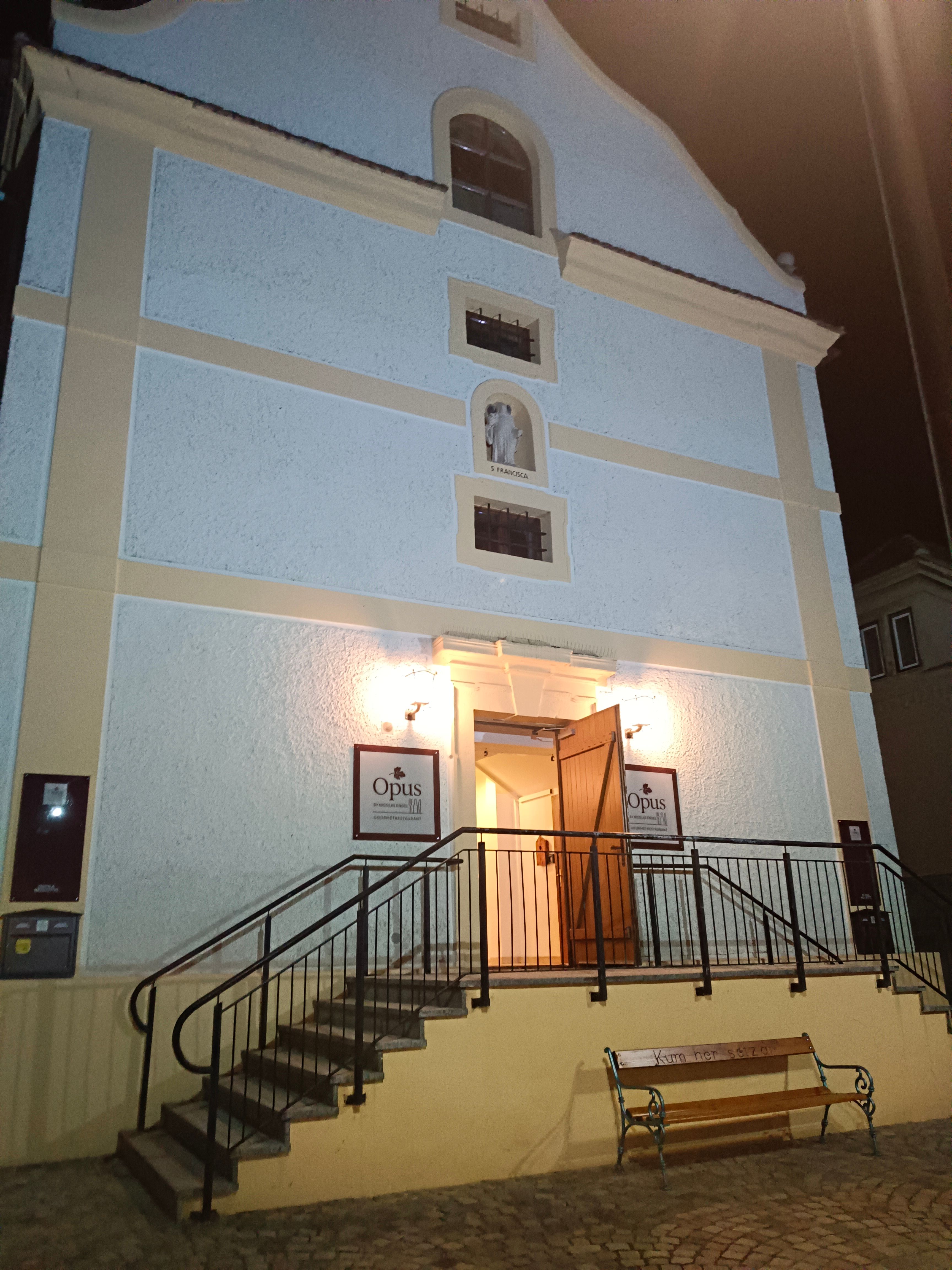 Eingang eines Gebäudes mit Treppe und geöffneten Türen, beleuchtet bei Nacht.