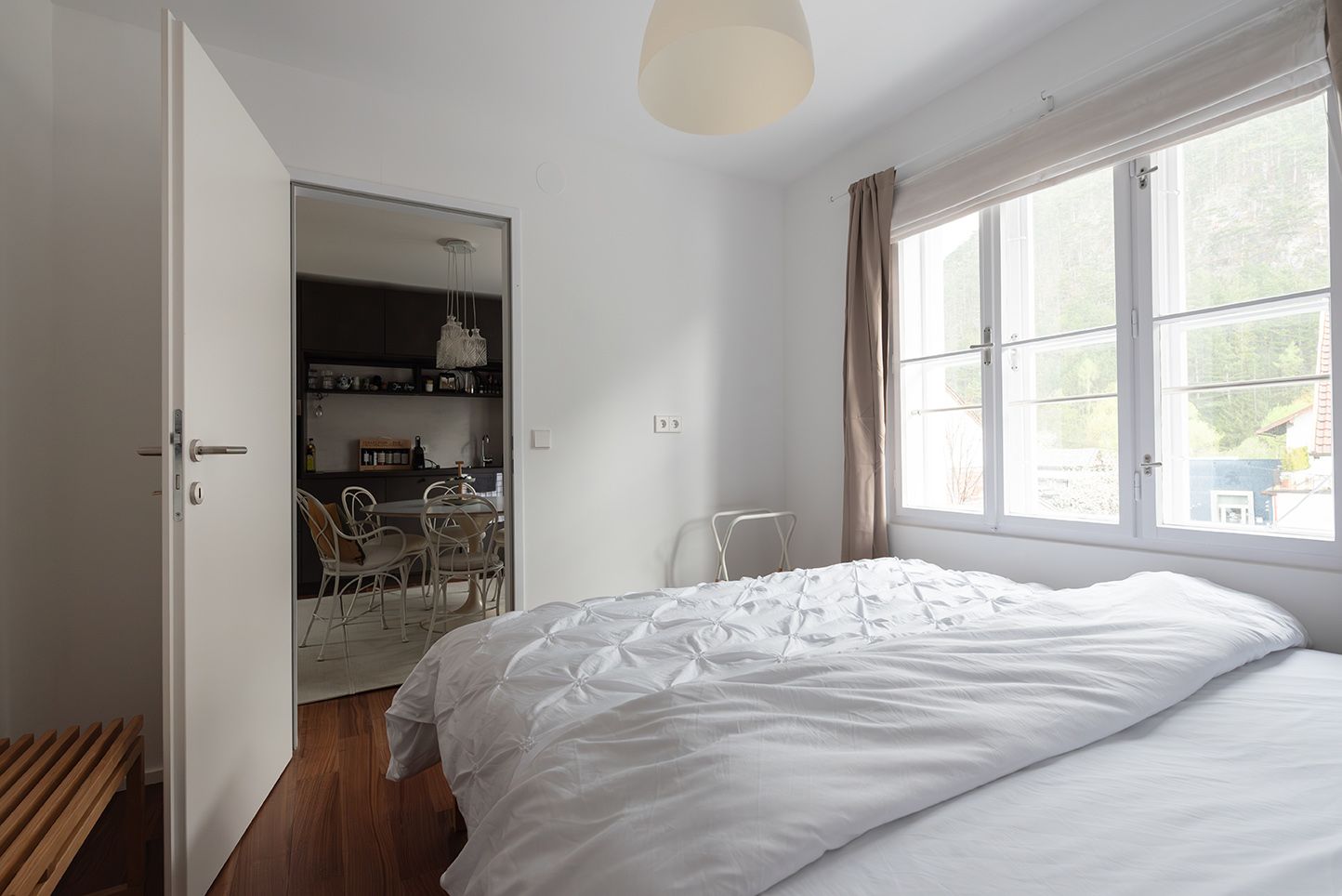 Ein helles Schlafzimmer mit einem großen Fenster, das auf eine Küche mit Esstisch und Stühlen blickt.