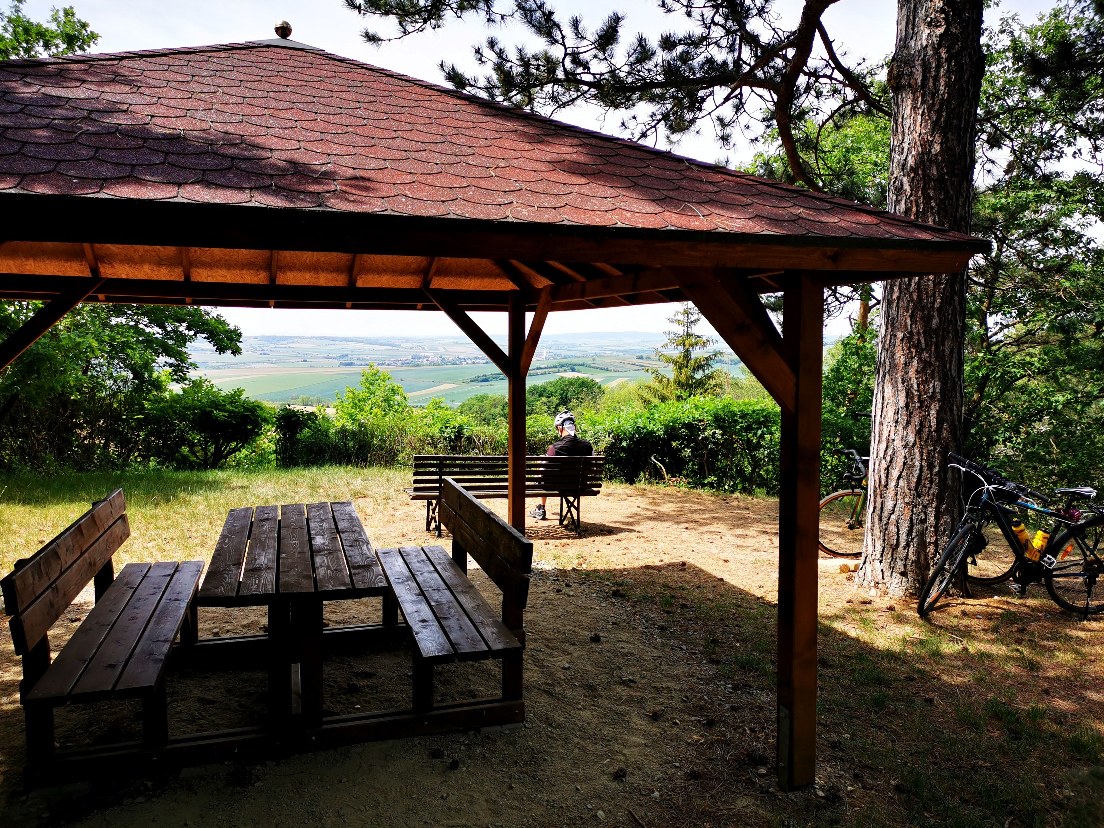 Holzpavillon mit Tisch und Bänken, Blick auf Weinberge, Fahrrad an einem Baum.