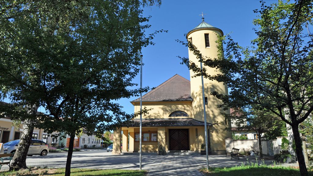 Antoniuskirche in Bad Erlach mit gelbem Turm und Bäumen im Vordergrund.