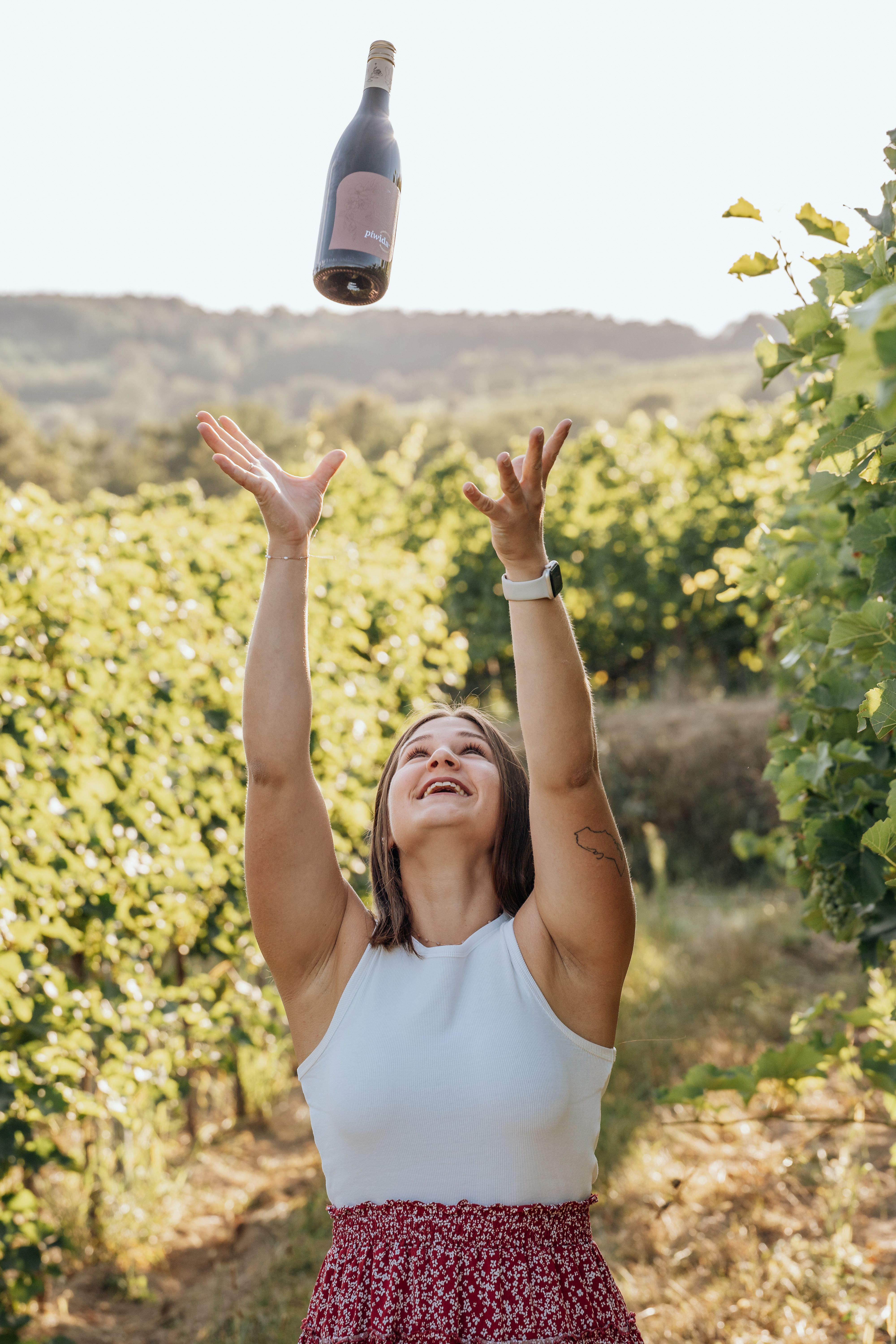Frau wirft Weinflasche in die Luft in einem Weinberg.