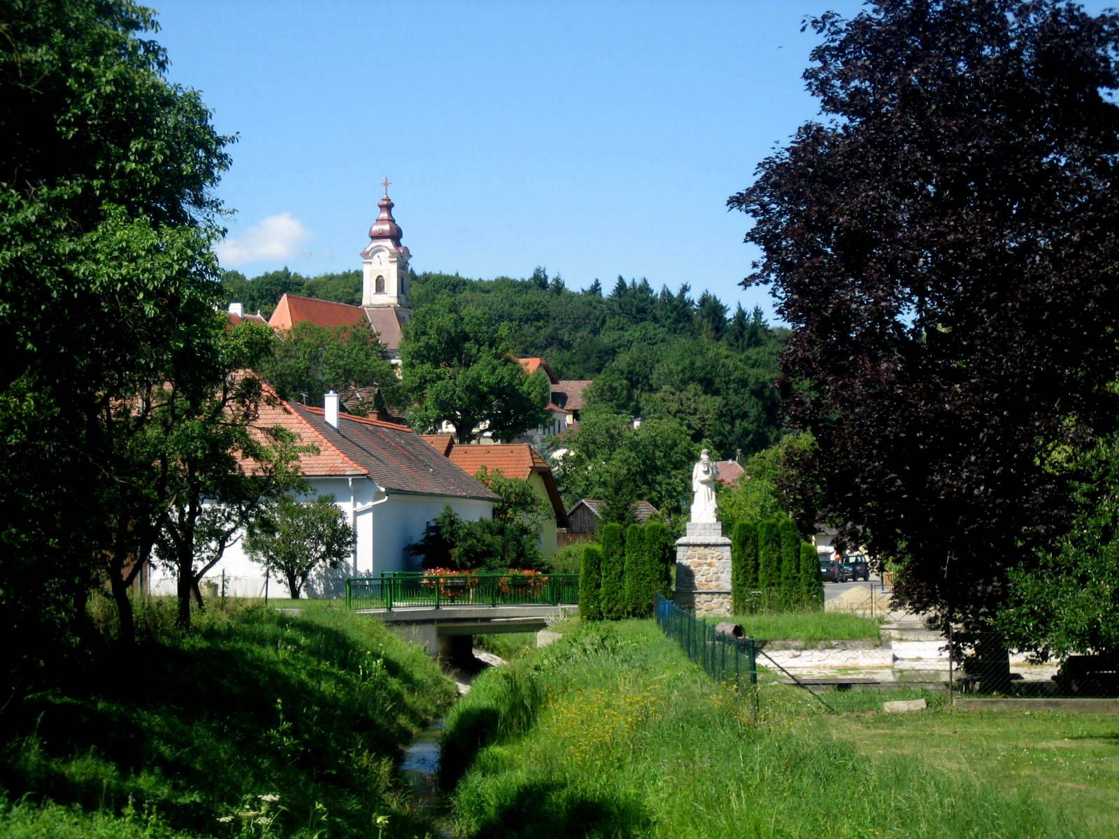 Landschaft mit Kirche und Statue in einem Dorf.