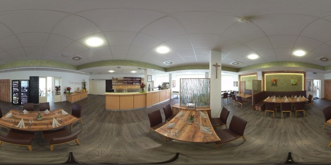 Innenansicht eines modernen Restaurants mit Holztischen und Stühlen, dekoriert mit Pflanzen und Kunstwerken an den Wänden.