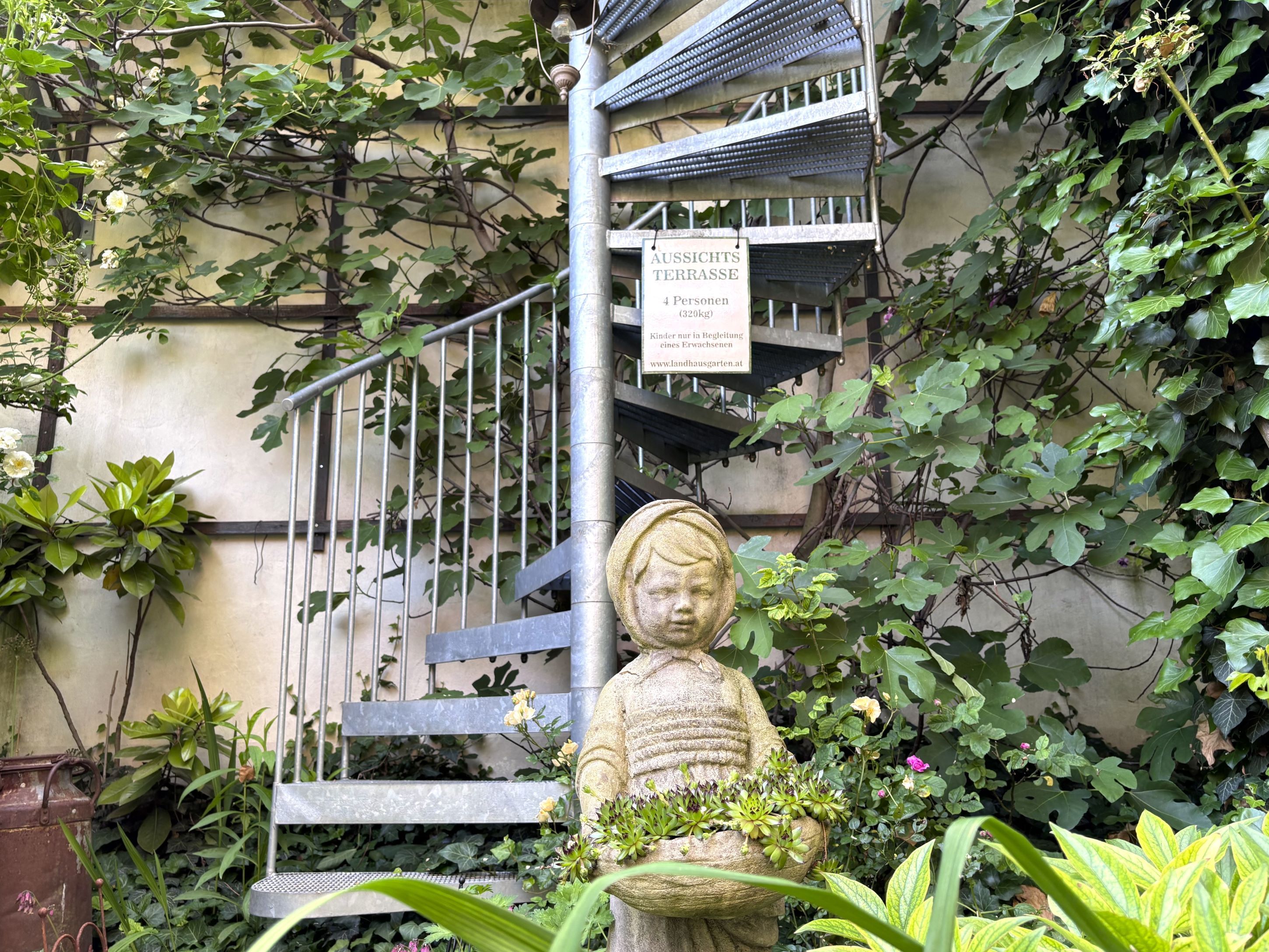 Steintreppe im Garten mit Pflanzen und Statue eines Kindes.