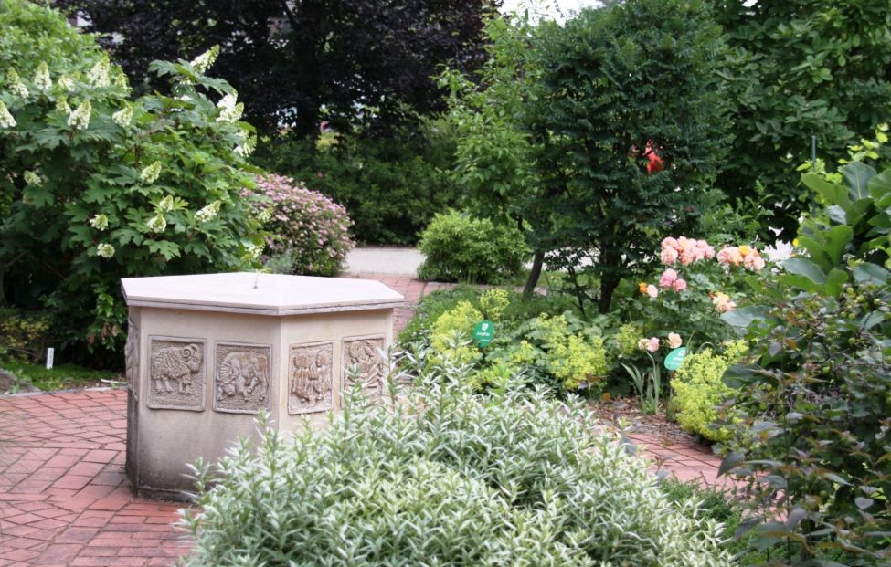 Ein gepflegter Garten mit einem steinernen Brunnen und blühenden Pflanzen.