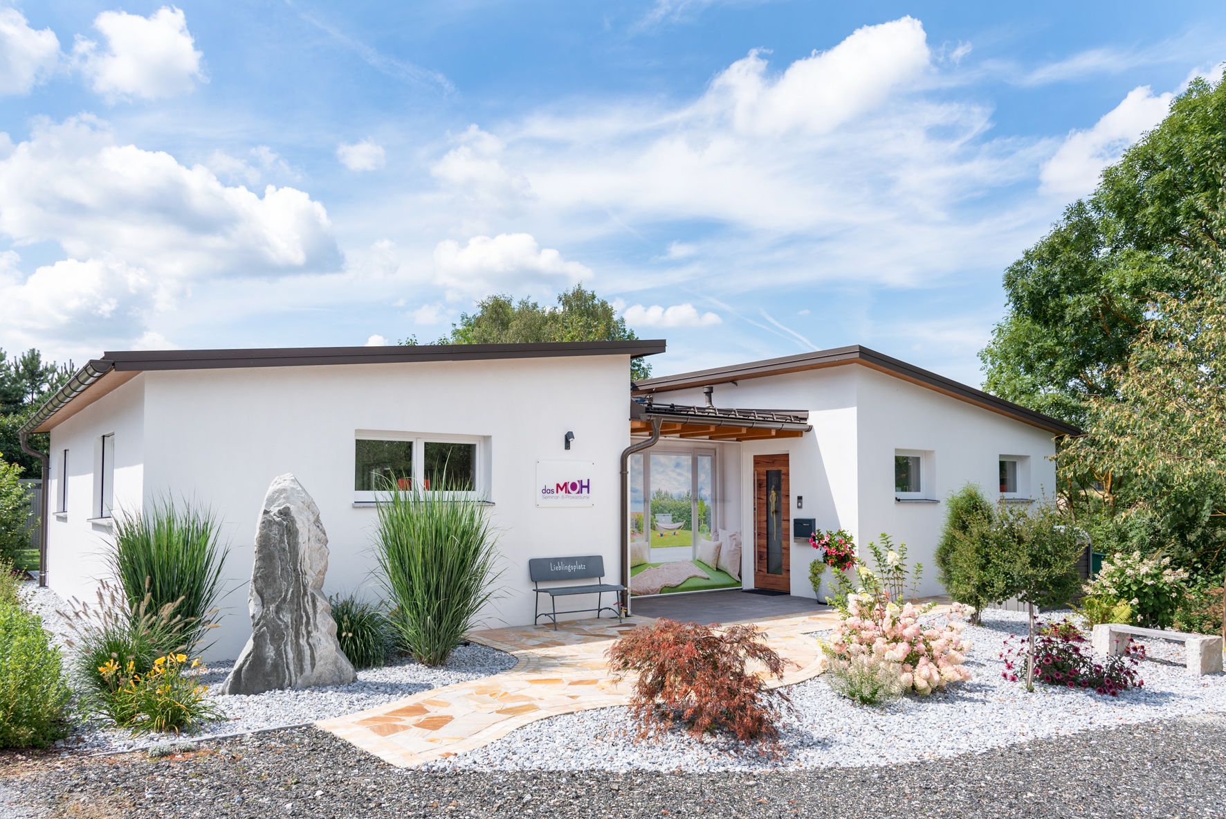 Modernes, weißes Gebäude mit Garten und Kiesweg, blauer Himmel im Hintergrund.