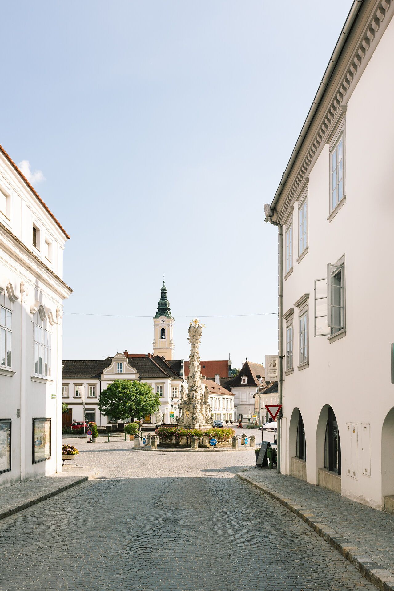 Ein malerischer Platz lädt zum Verweilen ein, umgeben von charmanten Gebäuden und einem beeindruckenden Brunnen. Die sanften Hügel im Hintergrund versprechen unvergessliche Ausblicke und laden zu Erkundungstouren in der Natur ein.