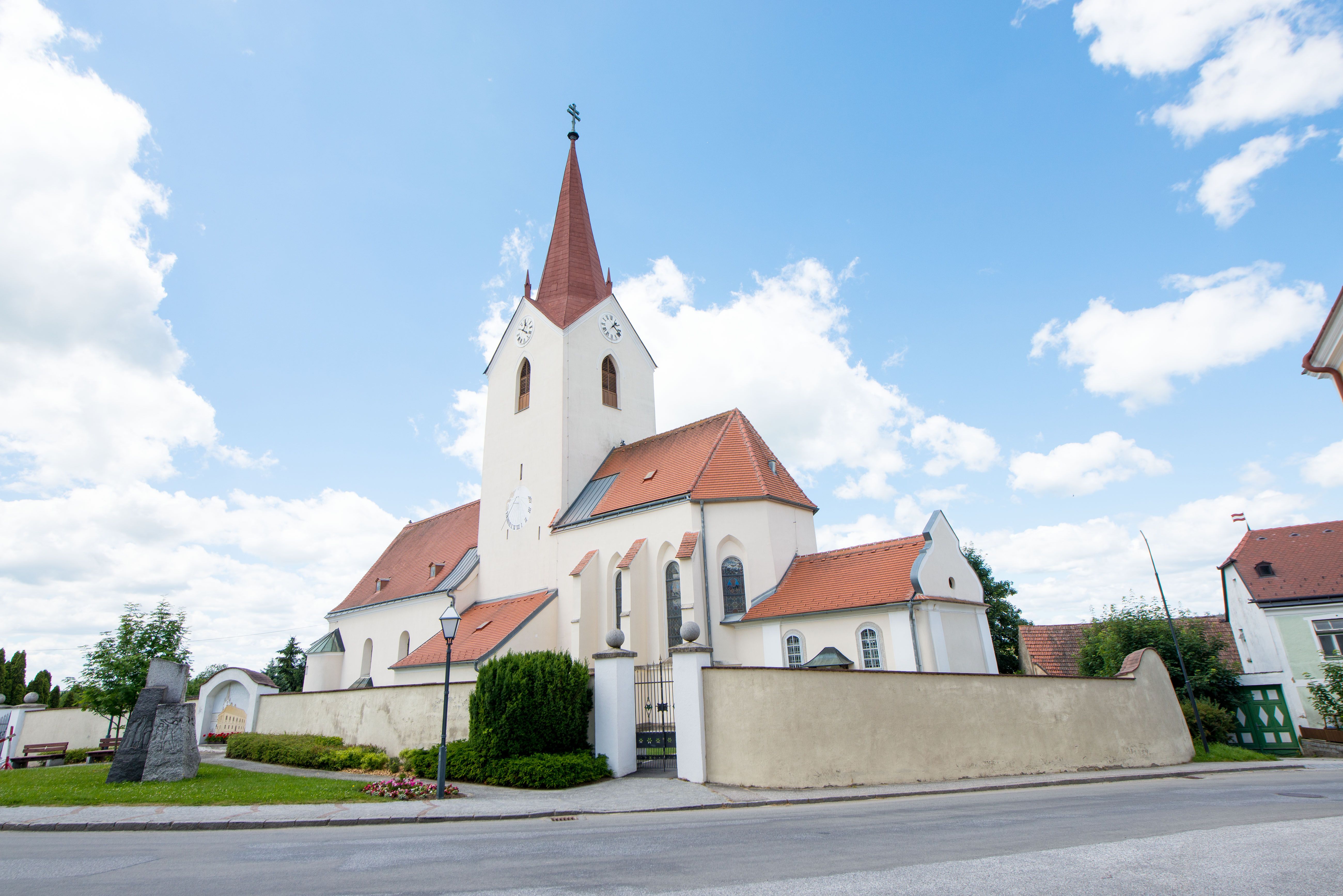 Kirche in Schweiggers mit rotem Dach und Turm vor blauem Himmel.