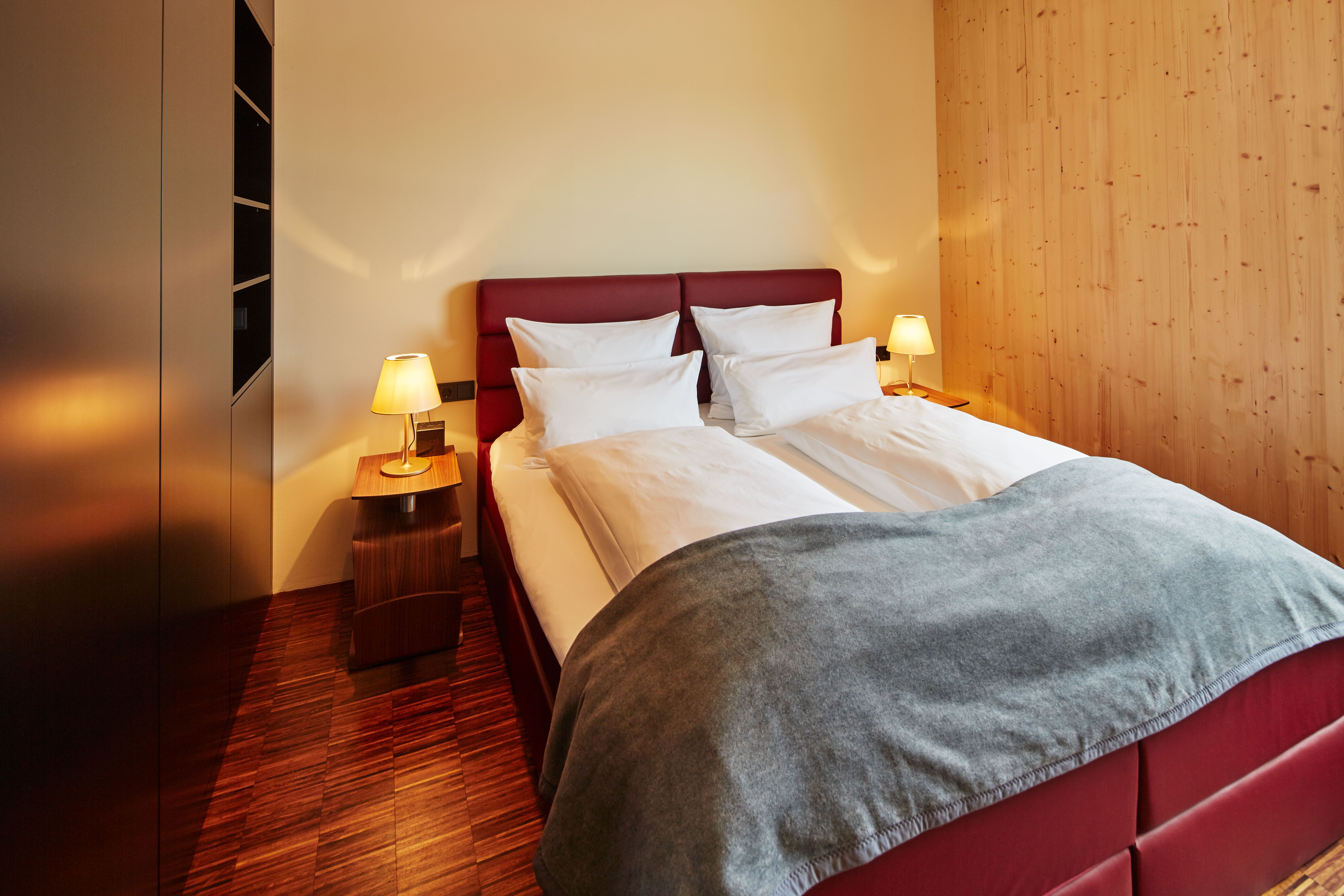 Ein gemütliches Schlafzimmer mit einem Doppelbett, roten Kopfteil, zwei Nachttischen mit Lampen und Holzwänden.
