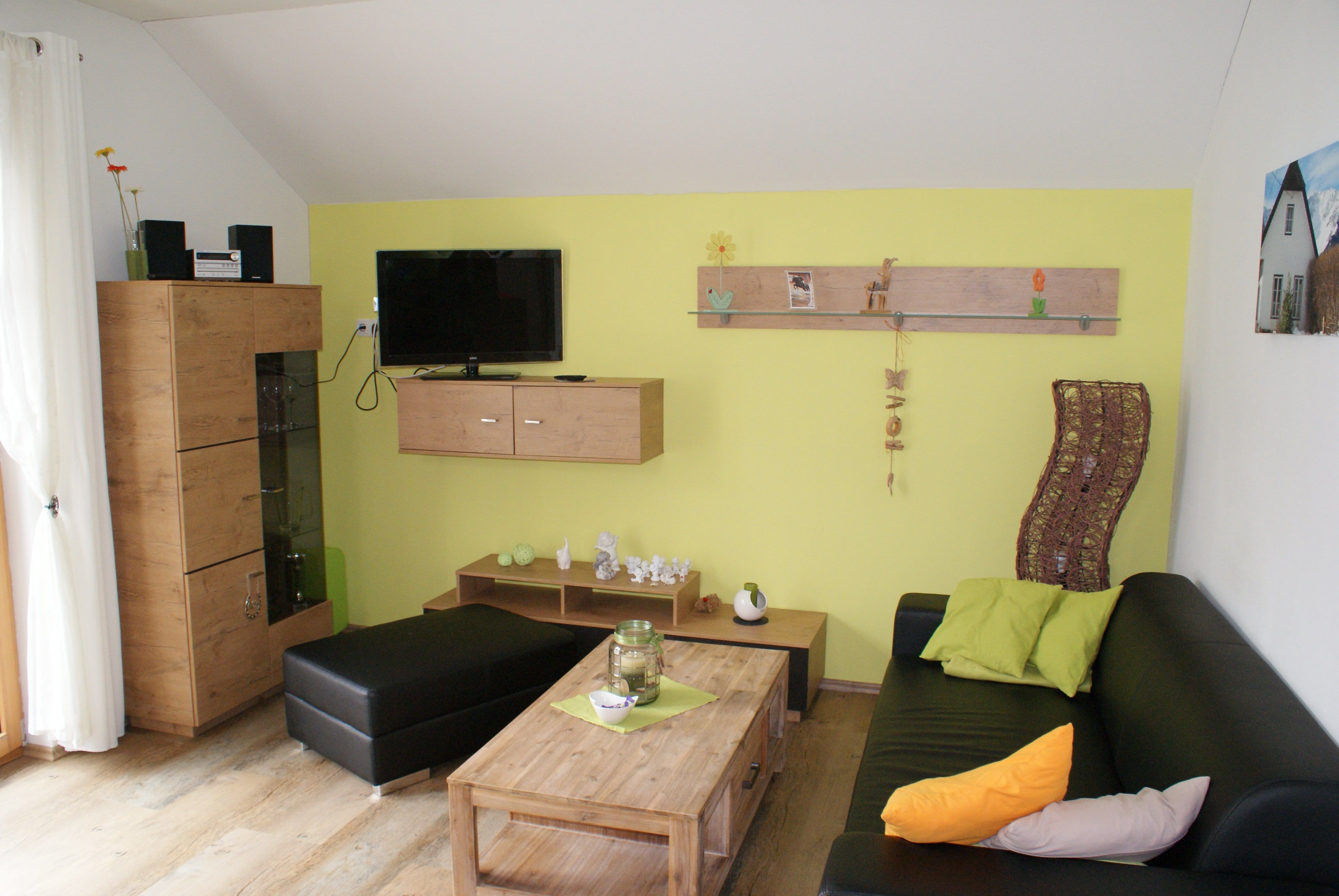 Modernes Wohnzimmer mit gelber Wand, schwarzem Sofa, Holzmöbeln und Dekorationen.