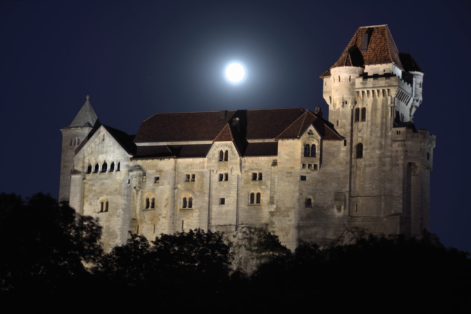 Burg Liechtenstein bei Nacht mit Vollmond im Hintergrund.