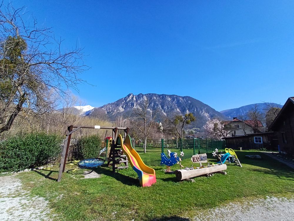 Kinderspielplatz mit Rutsche und Schaukel vor Bergkulisse.