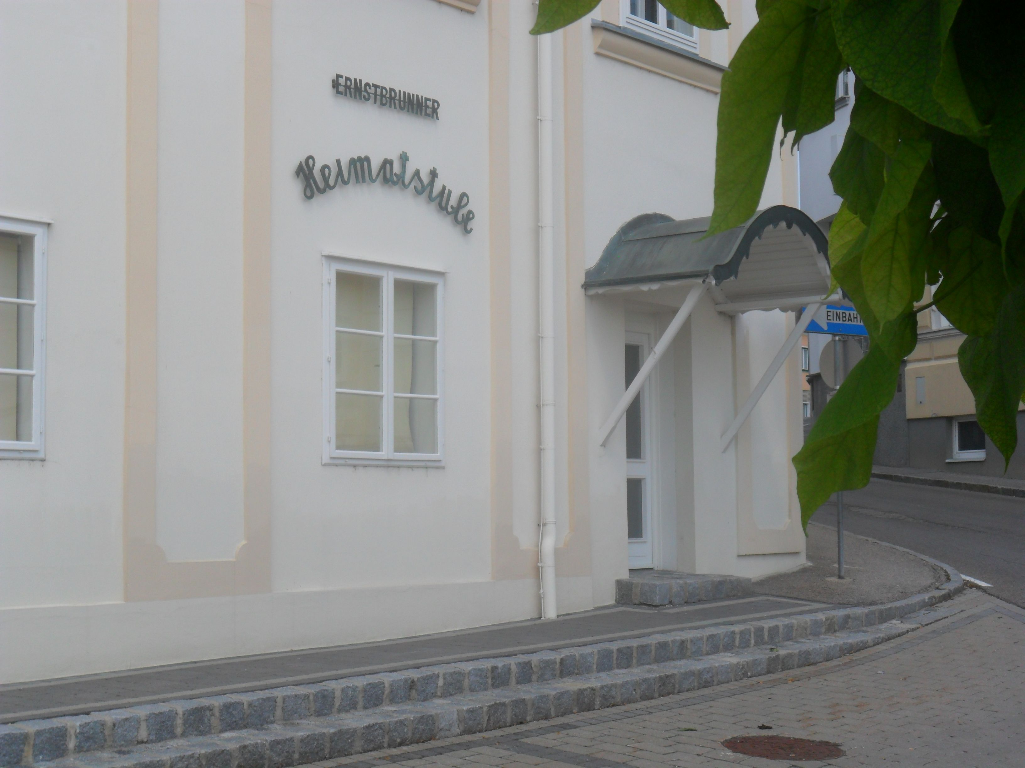 Eingang zur Ernstbrunner Heimatstube mit Vordach und Straßenschild.