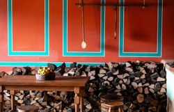 Innenaufnahme eines römischen Hauses mit roter Wand, Holztisch und Holzsessel.