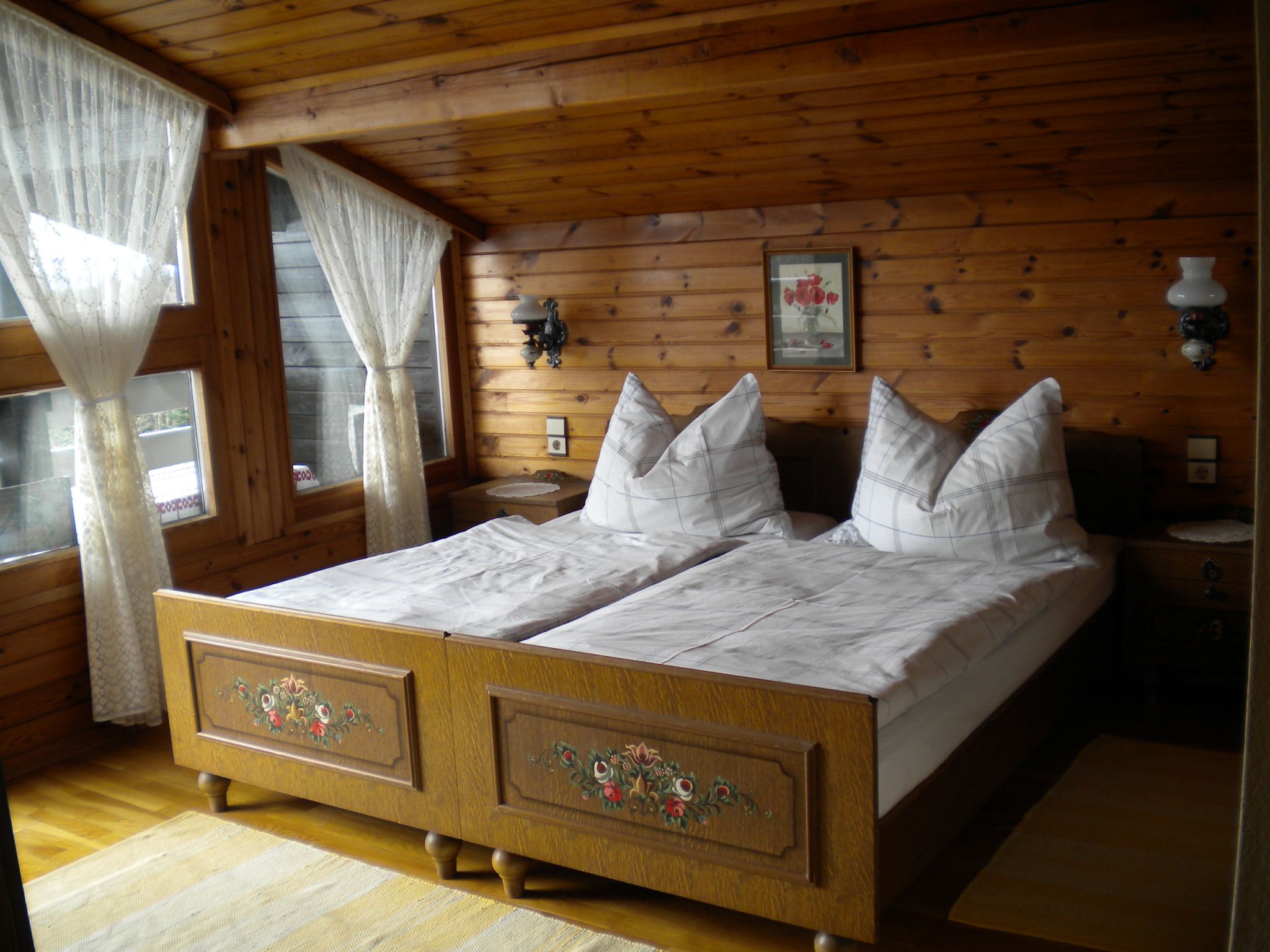 Gemütliches Schlafzimmer mit Holzwänden, Doppelbett und Spitzengardinen.