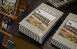 Mehrere Exemplare des Radguides „Der Weite Landguide“ liegen auf einem Tisch. Auf dem Cover ist eine Radfahrerin in einer vom Weinanbau geprägten Landschaft abgebildet.