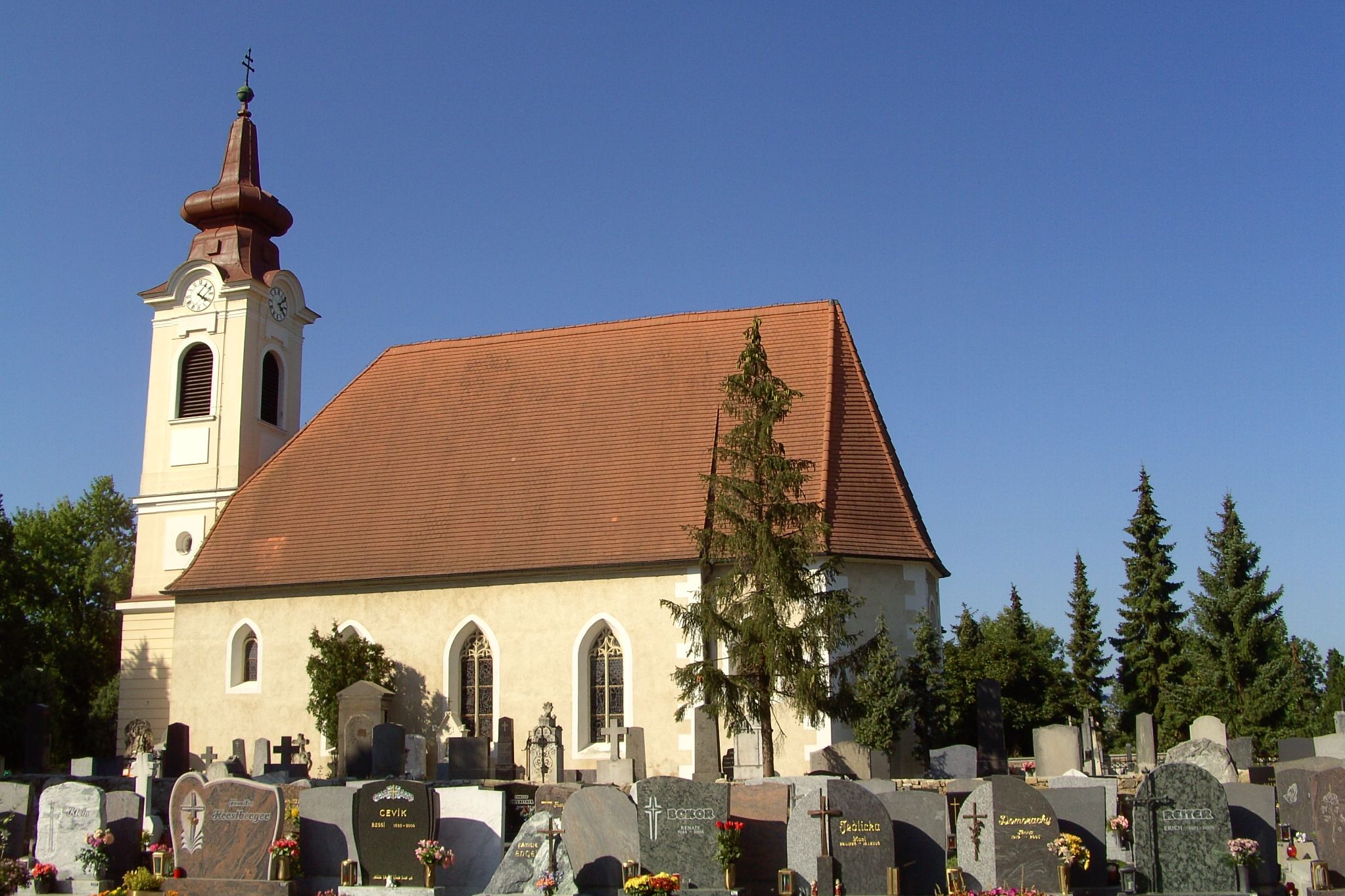 Außenansicht einer Kirche mit Friedhof im Vordergrund und blauem Himmel.