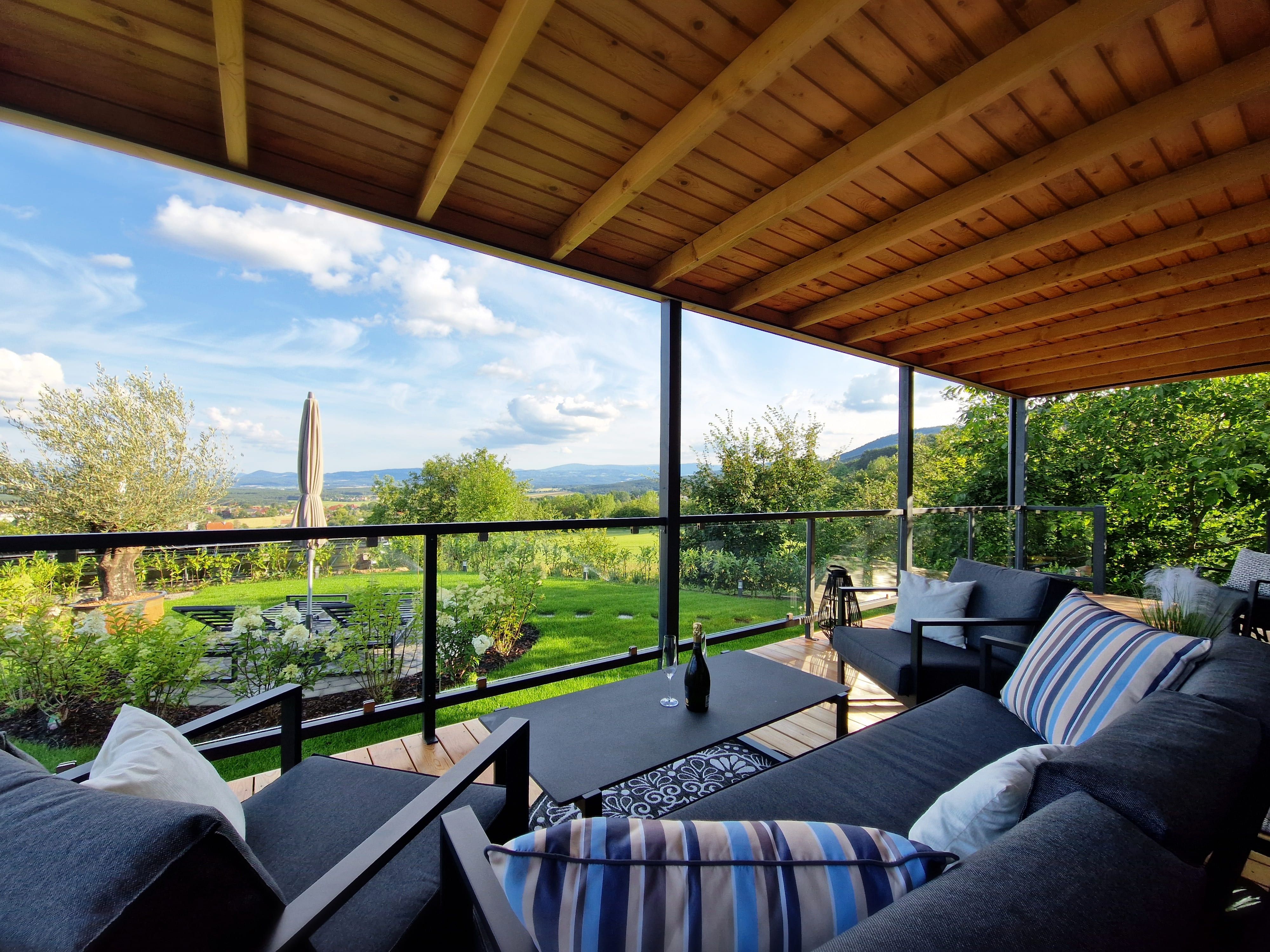 Überdachte Terrasse mit modernen Möbeln und Blick auf grüne Landschaft.