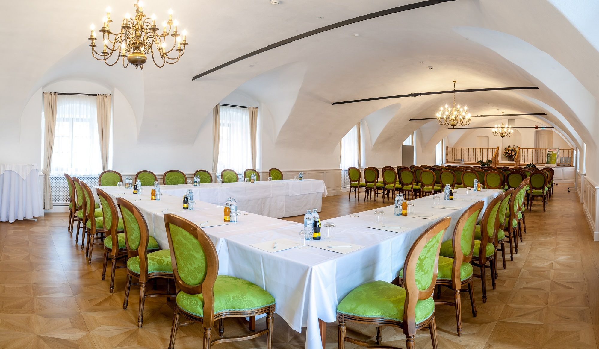 Eleganter Tagungsraum im Schloss Thalheim mit grünen Stühlen und Kronleuchtern.