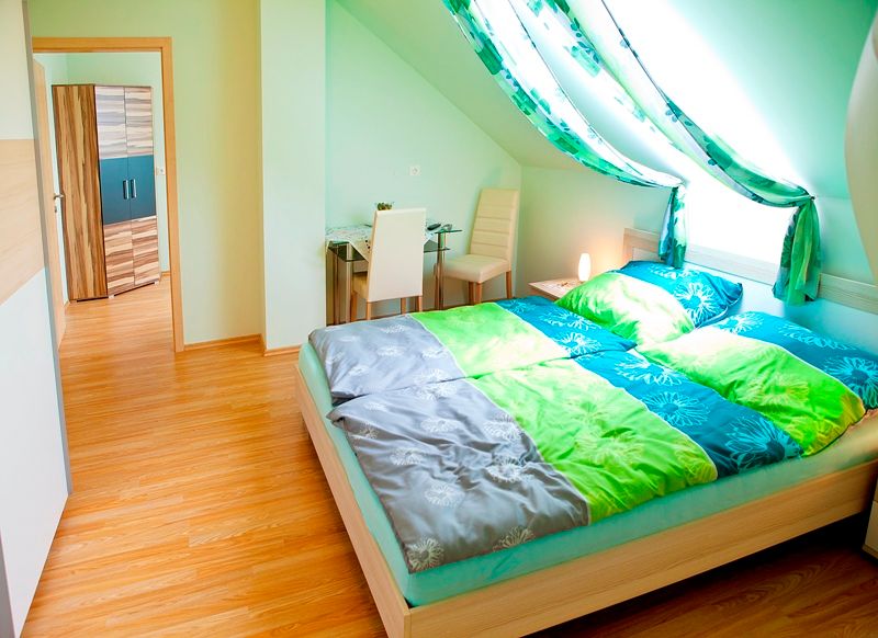 Helles Schlafzimmer mit Dachschräge, Doppelbett, Schreibtisch und Stuhl.