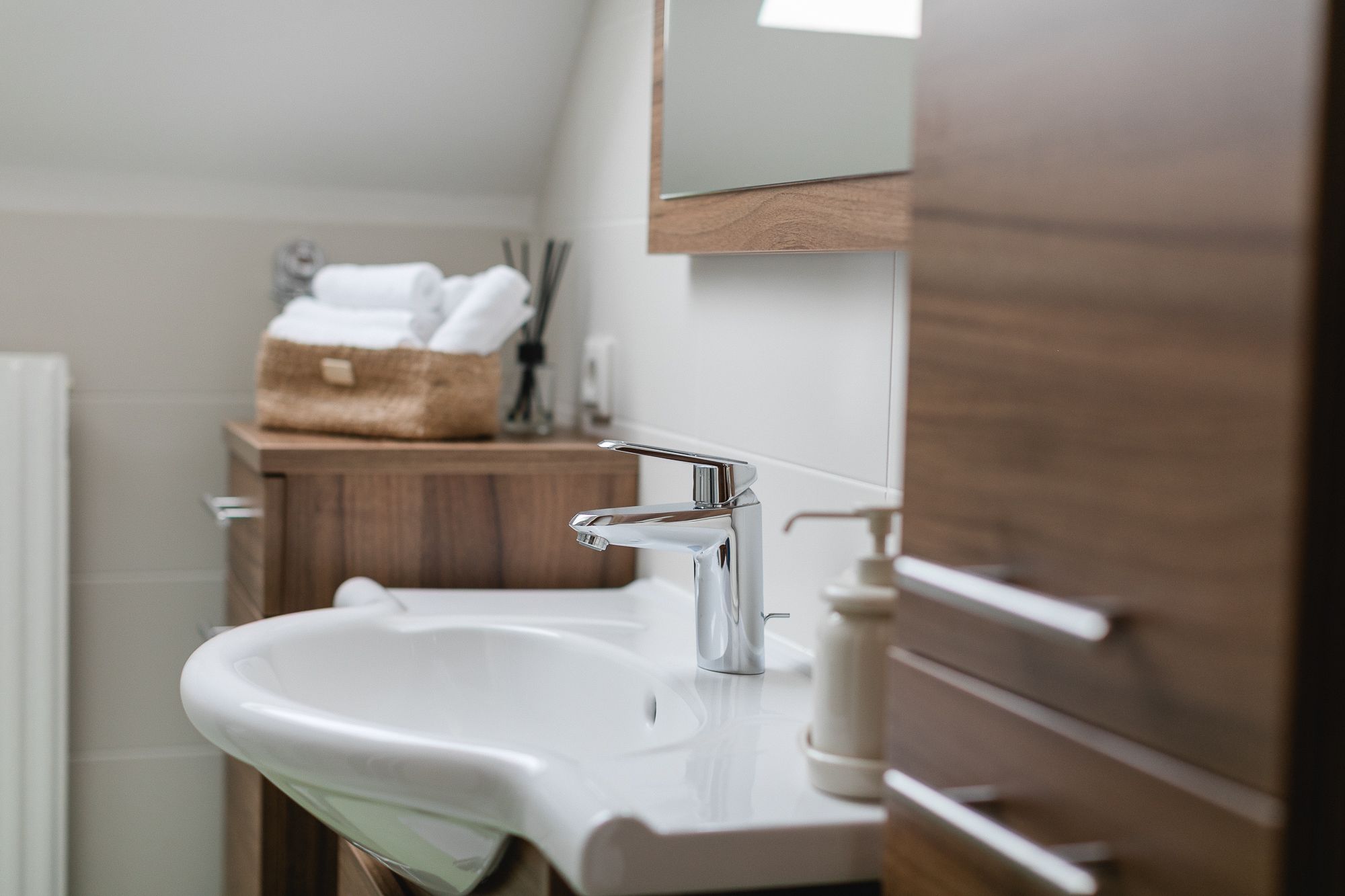 Modernes Badezimmer mit Waschbecken, Holzschränken und Handtüchern in einem Korb.