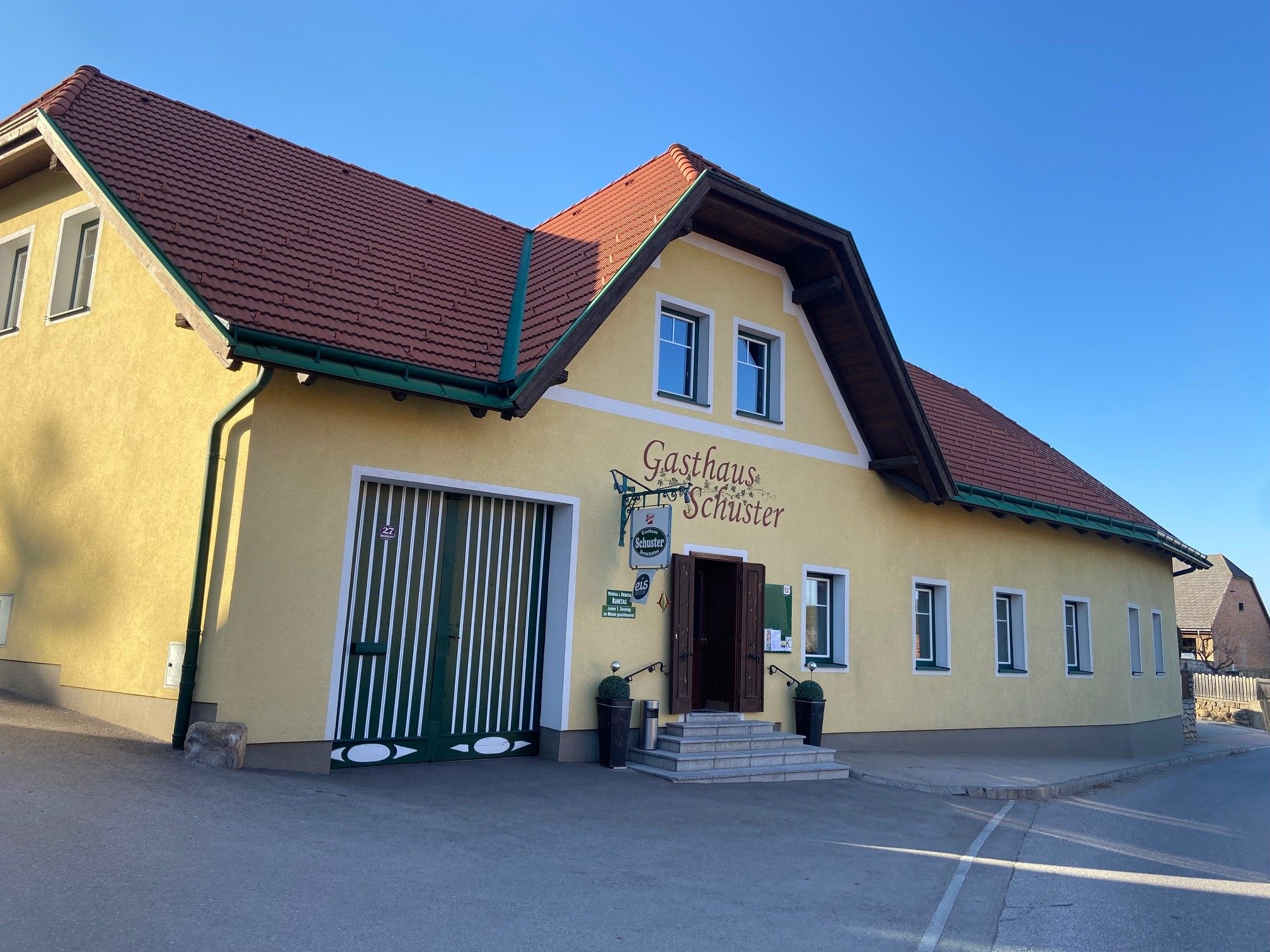 Gelbes Gebäude mit rotem Dach, beschriftet als Gasthaus Schuster.