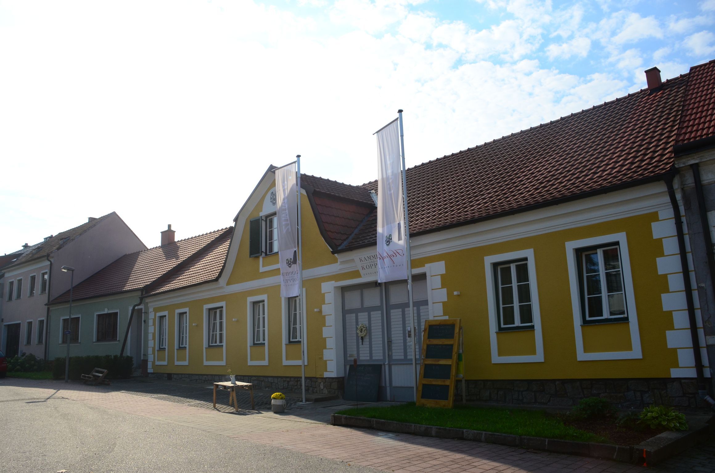 Gelbes Gebäude mit roten Dachziegeln und zwei Fahnen davor.