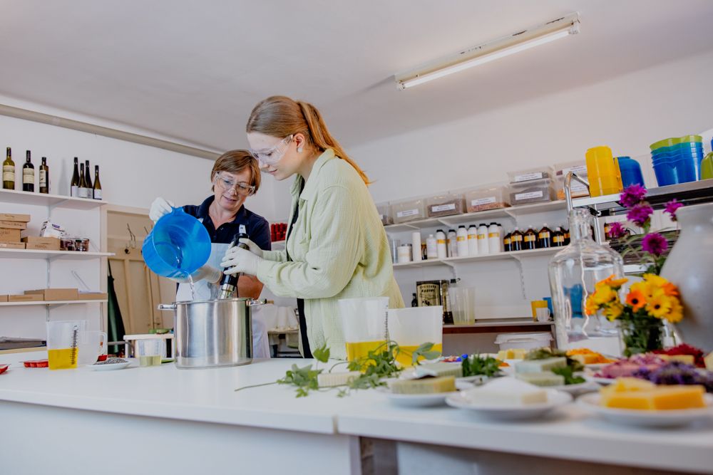 Zwei Personen stellen in einer Werkstatt Seife her, umgeben von Zutaten und Werkzeugen.