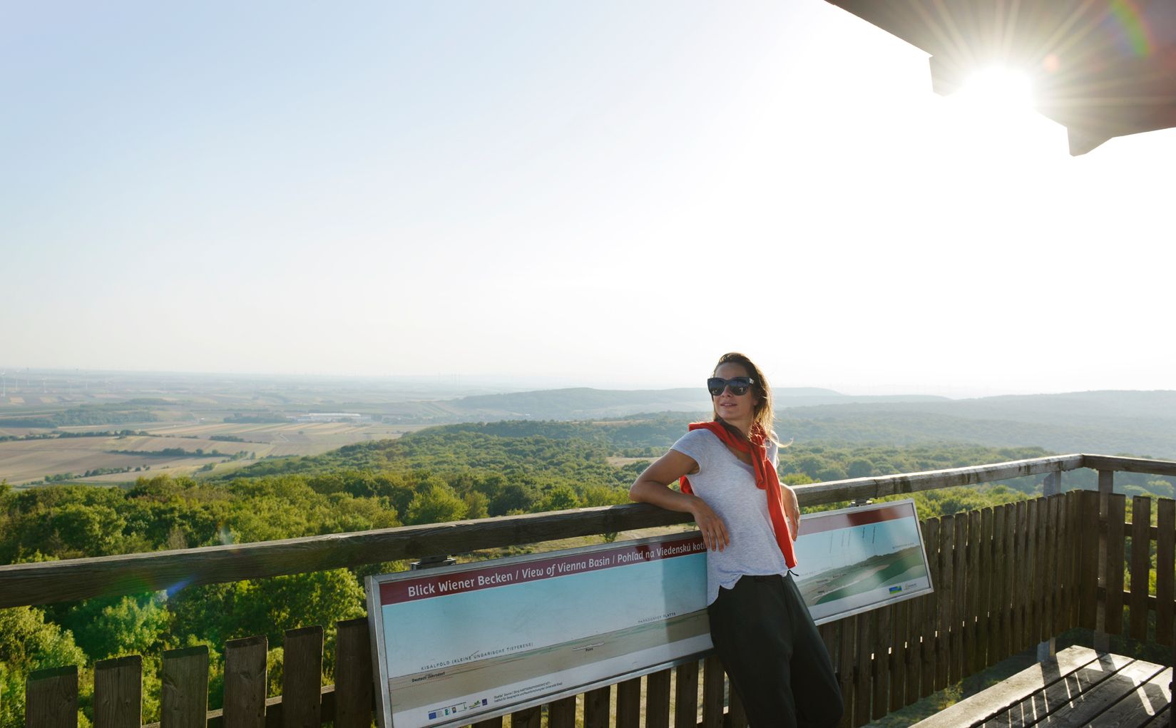 Frau mit Sonnenbrille lehnt an einem Geländer auf einem Aussichtsturm mit Blick auf eine weite Landschaft.
