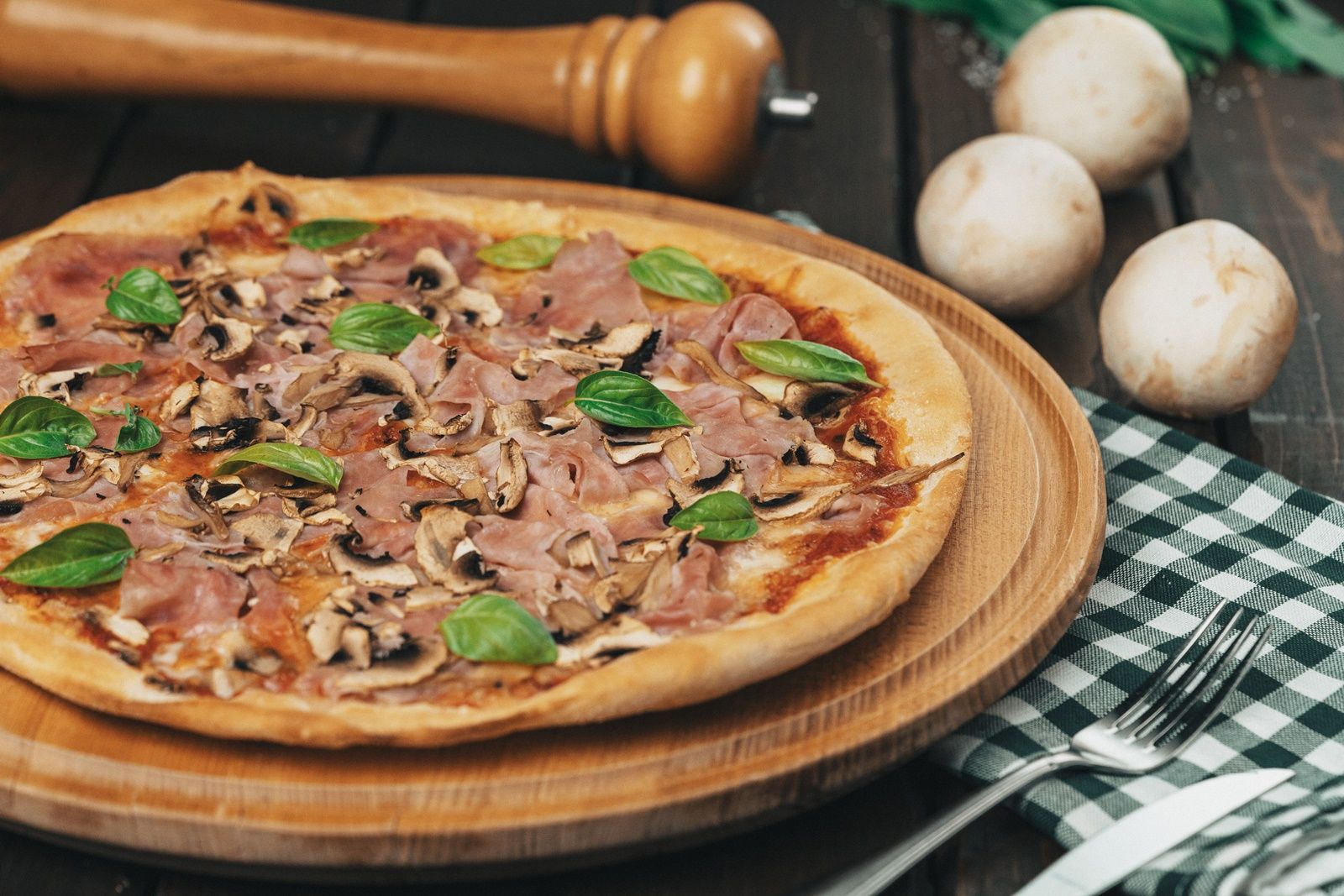 Pizza mit Schinken, Pilzen und Basilikum auf einem Holzbrett.
