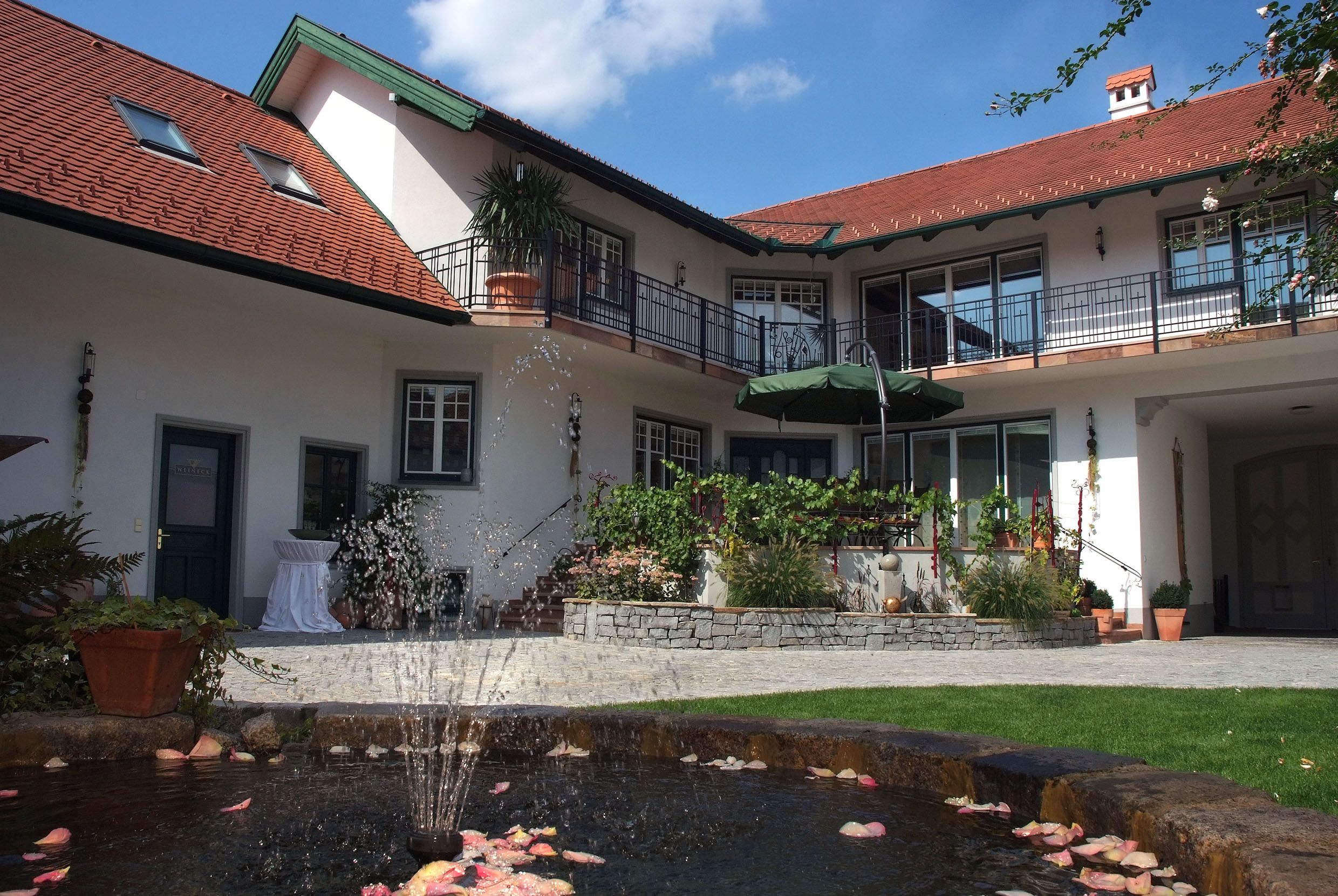 Ein Innenhof mit einem Brunnen, umgeben von einem zweistöckigen Gebäude mit roten Dächern und Balkonen.