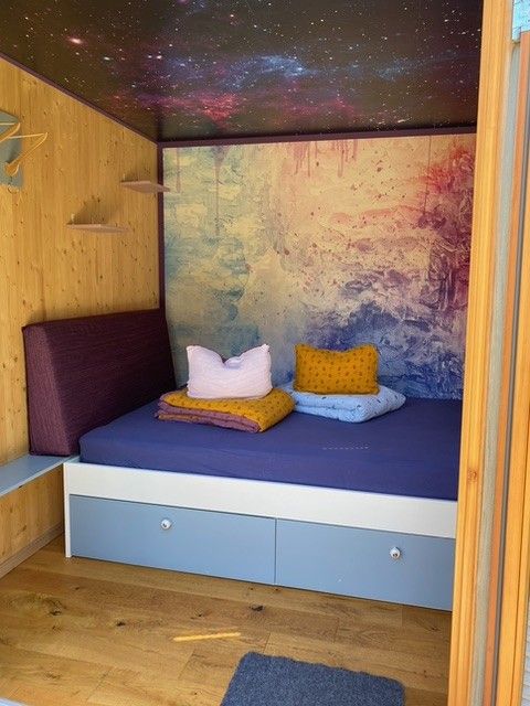 Kleines, gemütliches Zimmer mit einem Bett und bunten Kissen.