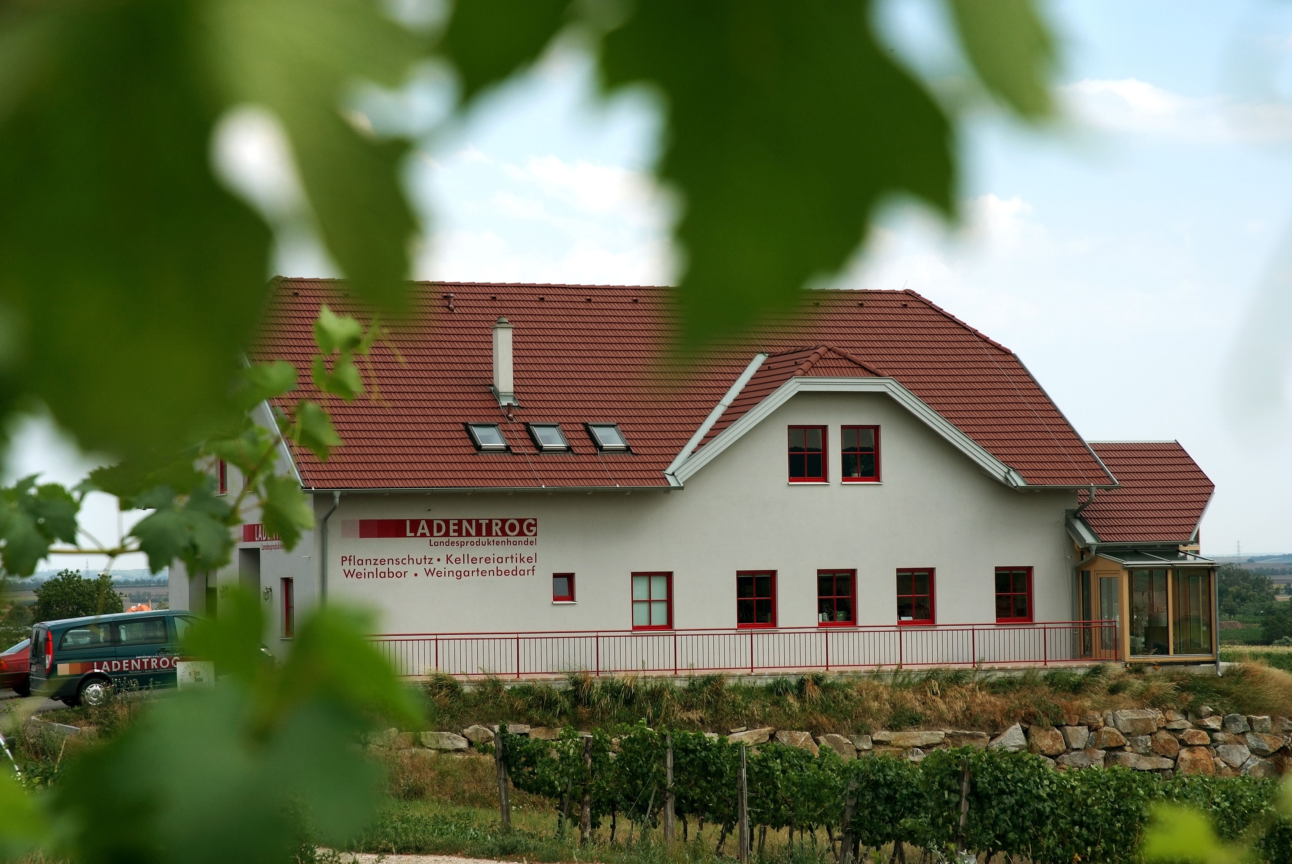 Gebäude mit rotem Dach und Schriftzug 'LADENTROG' in einer ländlichen Umgebung.
